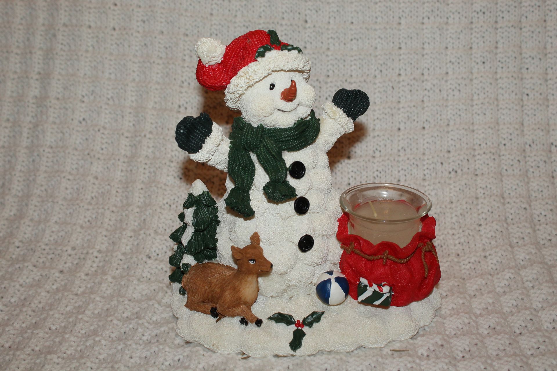 Snowman holiday decoration with red hat, green scarf, small dog, and candle holder on a beige surface