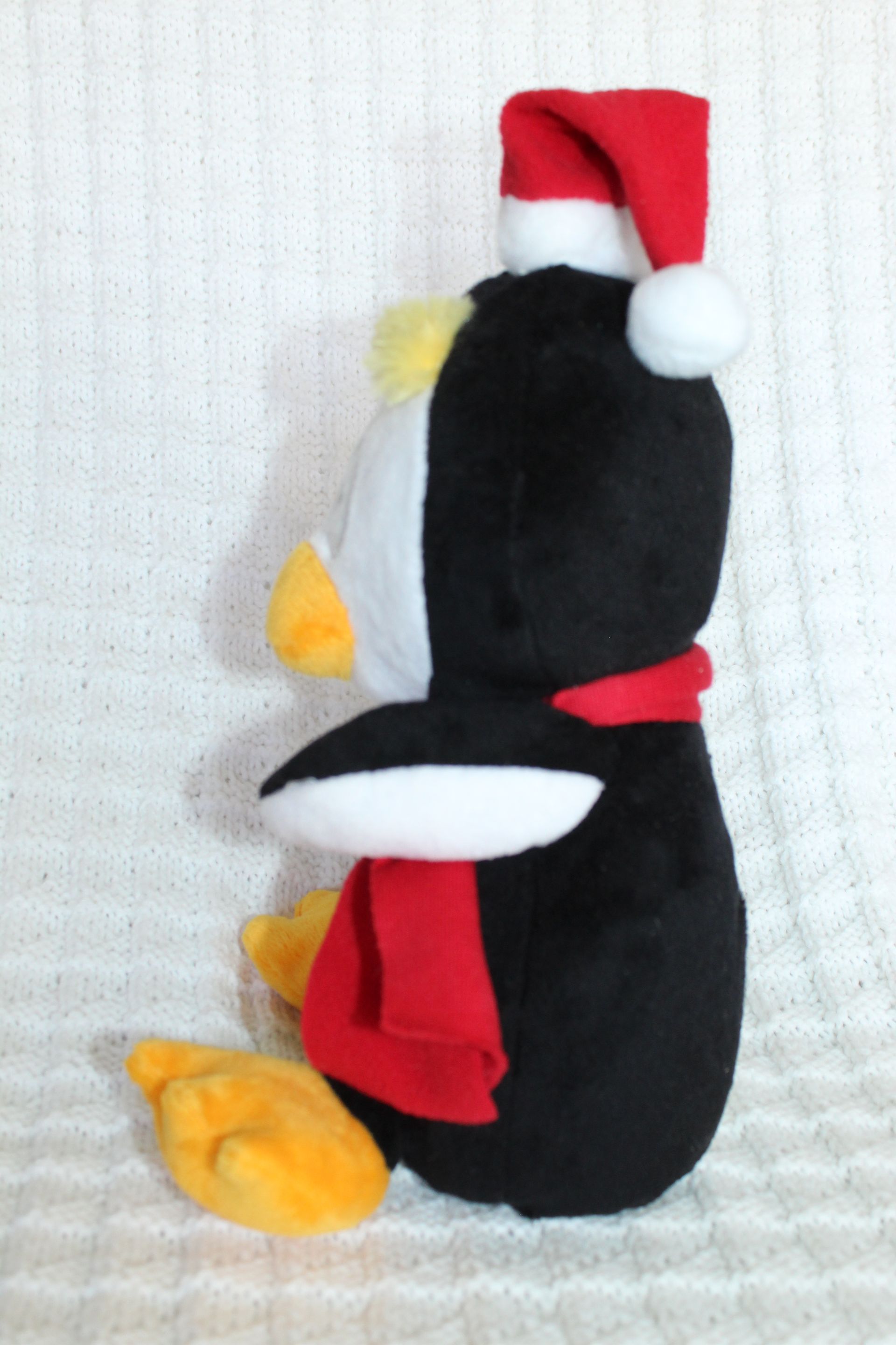 Black plush penguin wearing a red Santa hat and scarf, with white wings and yellow feet