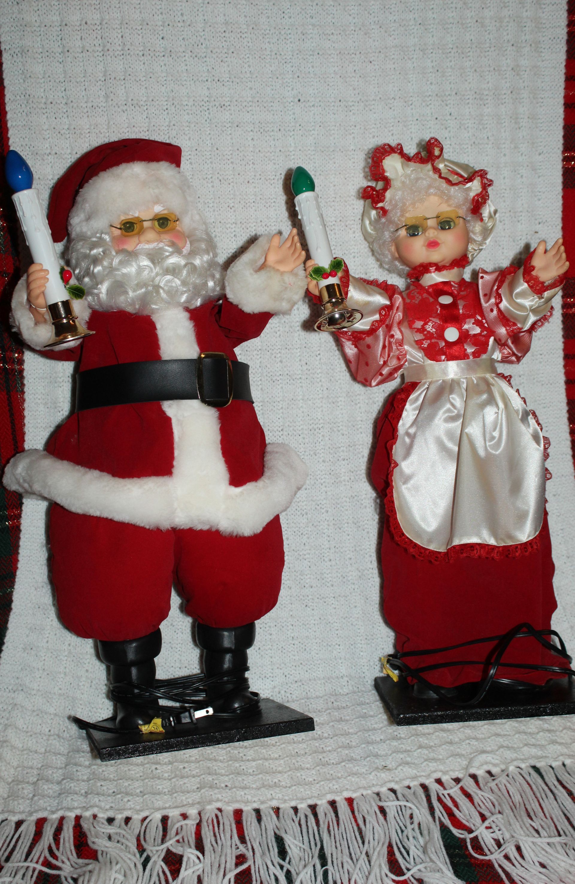 Santa and Mrs. Claus figurines in red outfits, each holding a candy cane, standing on black bases.