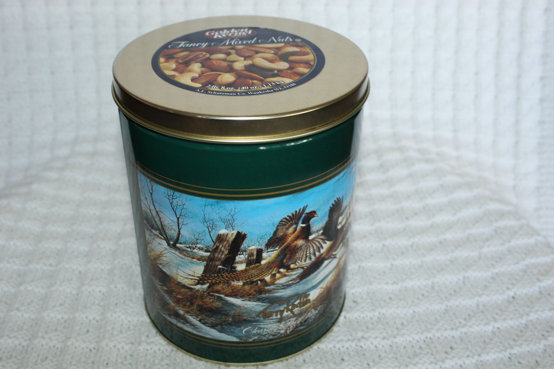 Decorative tin can with a winter shipwreck scene and gold lid on a white textured background