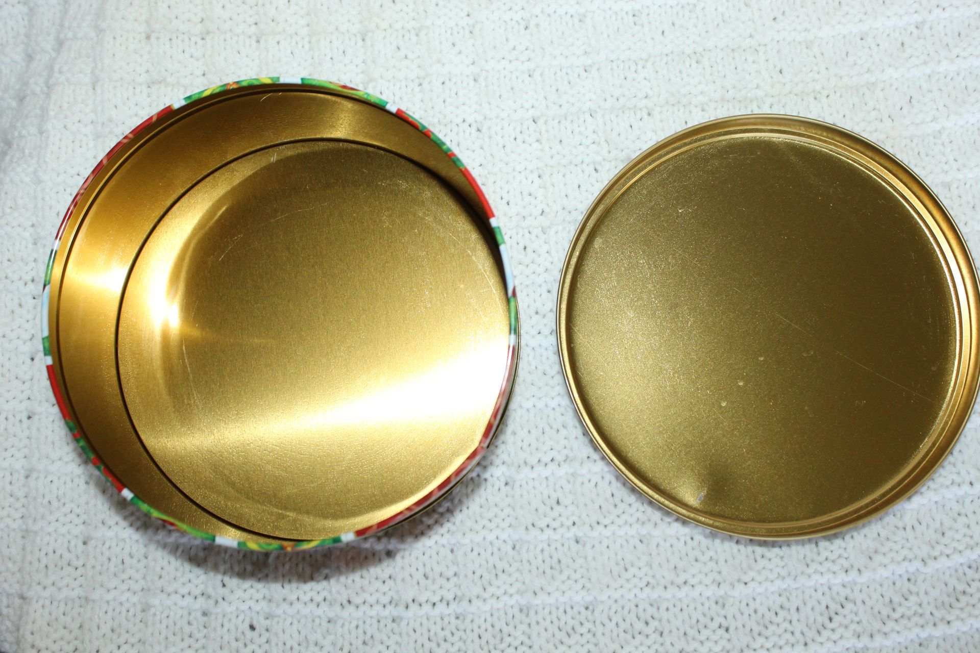 Festive red and green round gift tin with holiday patterns on a white textured surface