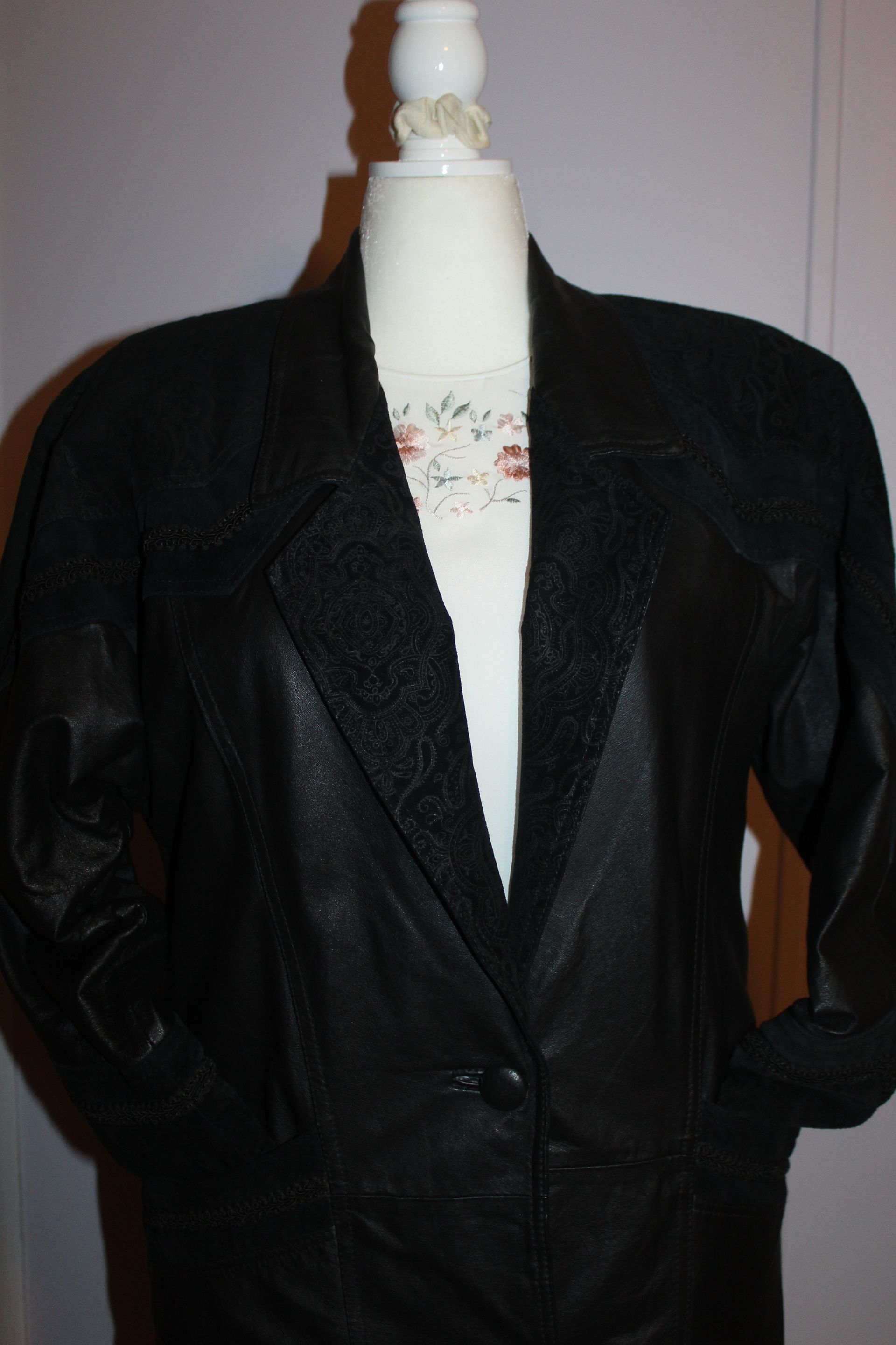 Black blazer on a dress form over a white top, shown against an indoor wall.
