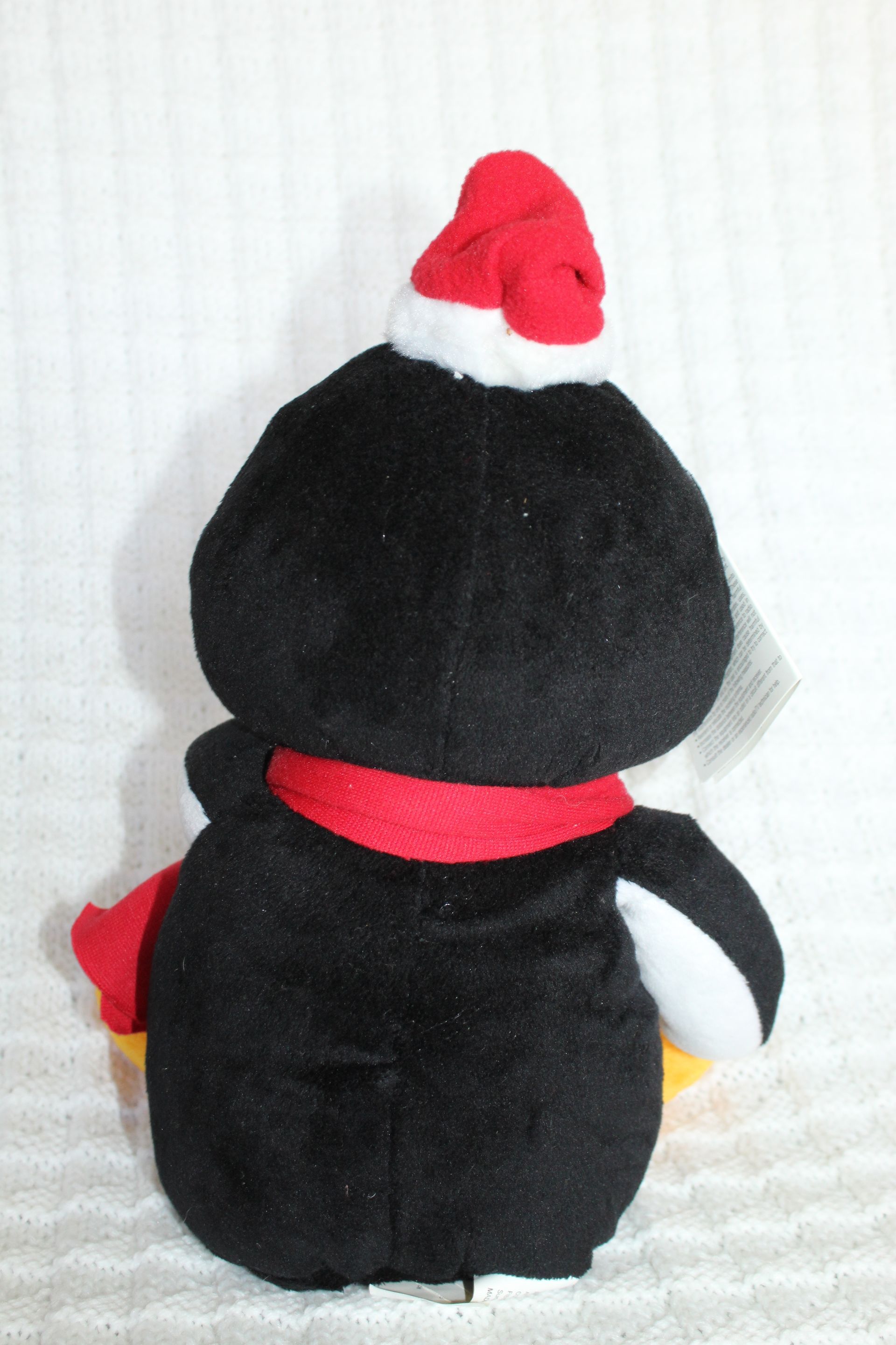 Black-and-white plush penguin wearing a red Santa hat and scarf, viewed from behind