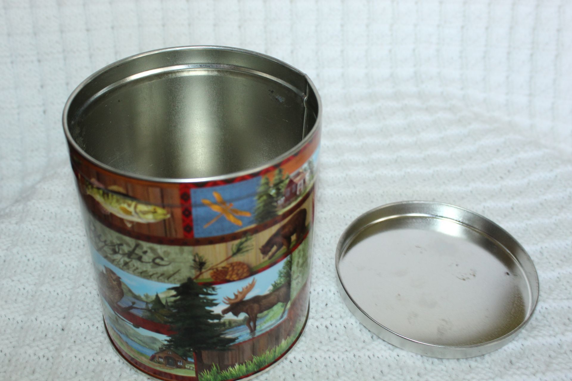 Decorative tin can with a winter shipwreck scene and gold lid on a white textured background