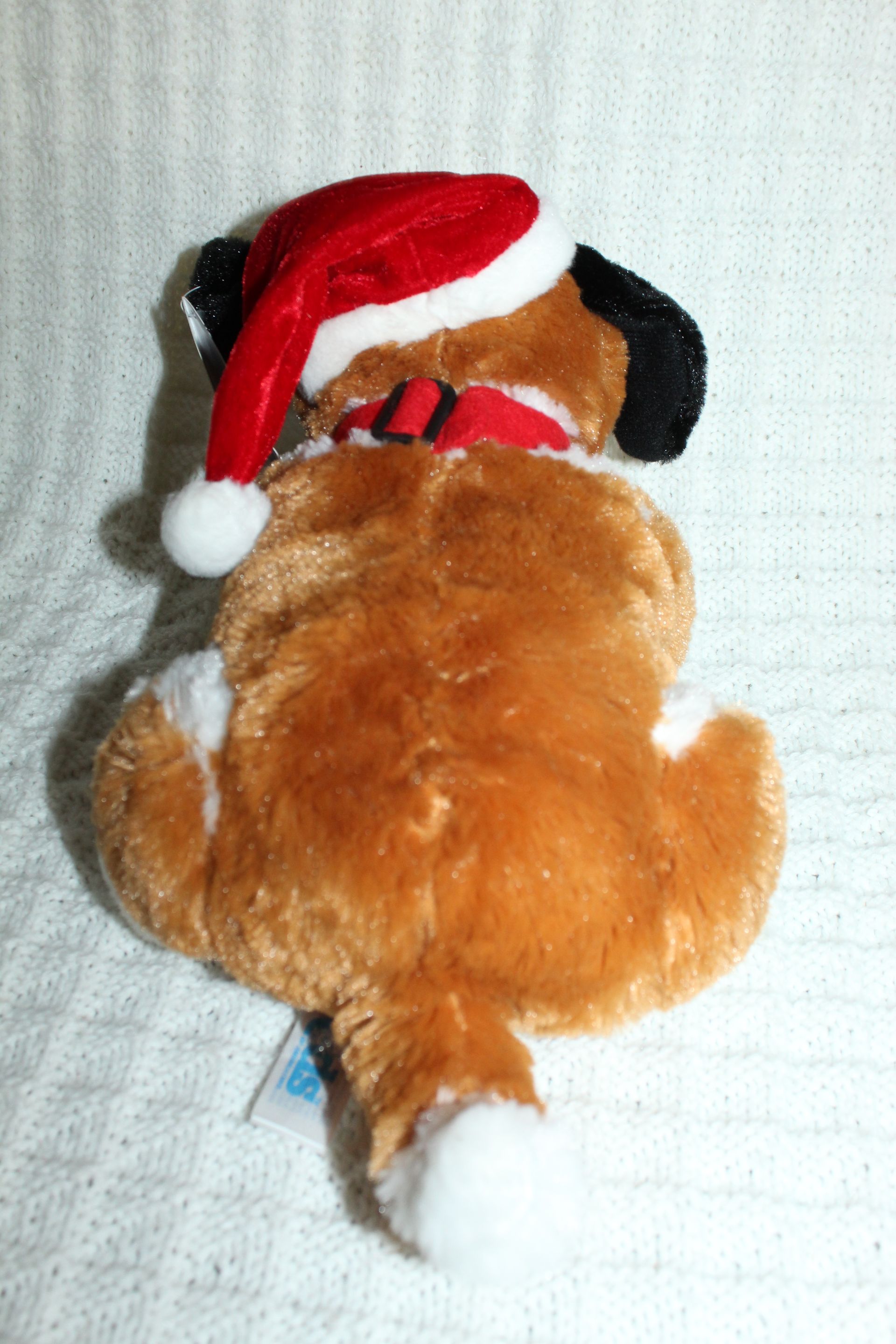 Plush St. Bernard puppy wearing a Santa hat on a white blanket