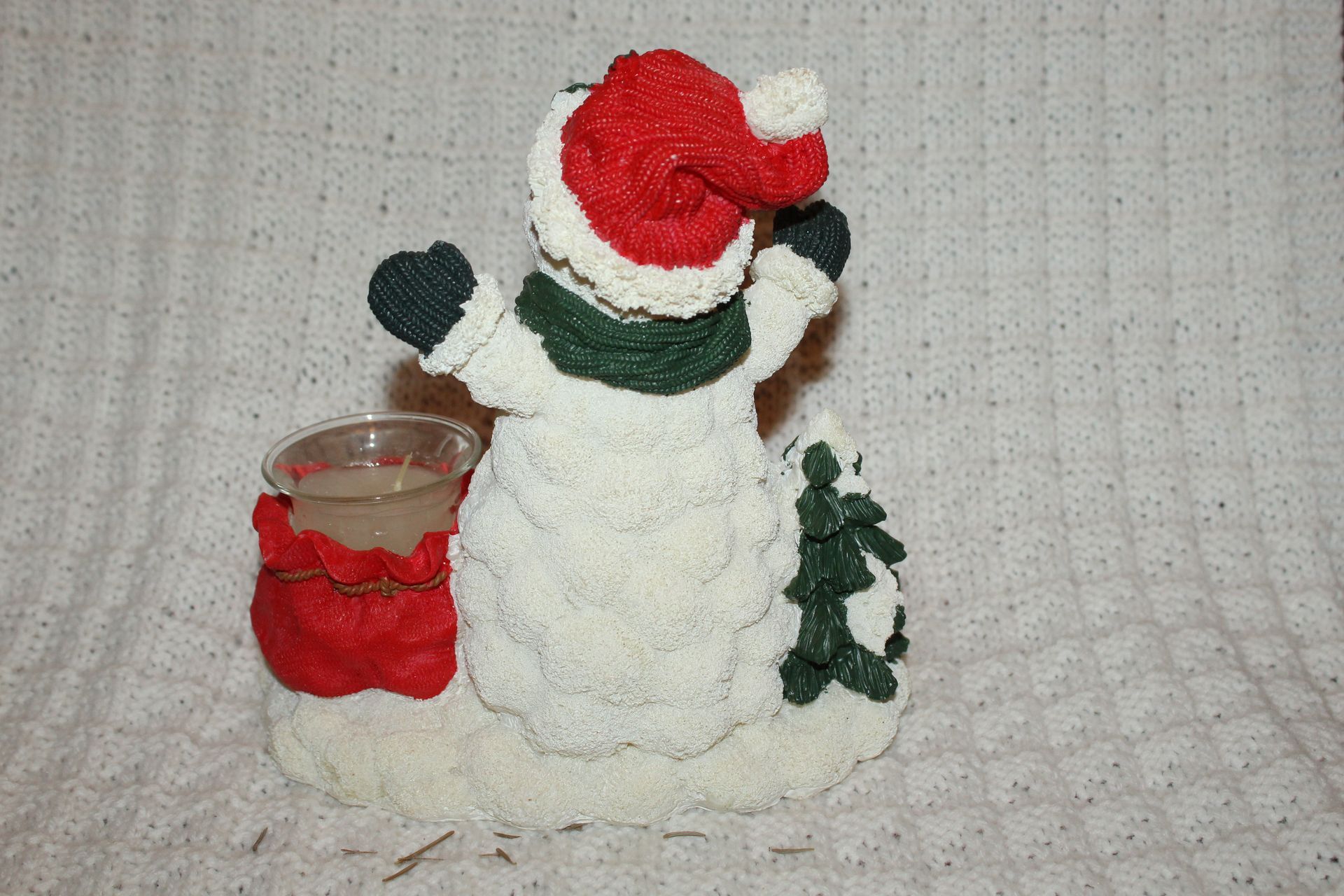 Snowman holiday decoration with red hat, green scarf, small dog, and candle holder on a beige surface
