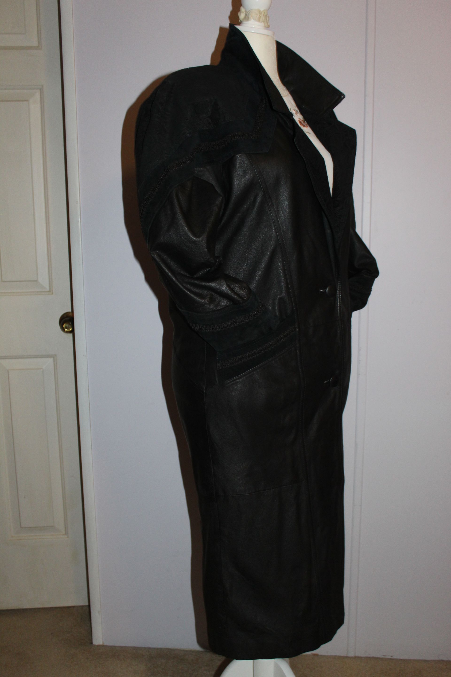 Black blazer on a dress form over a white top, shown against an indoor wall.