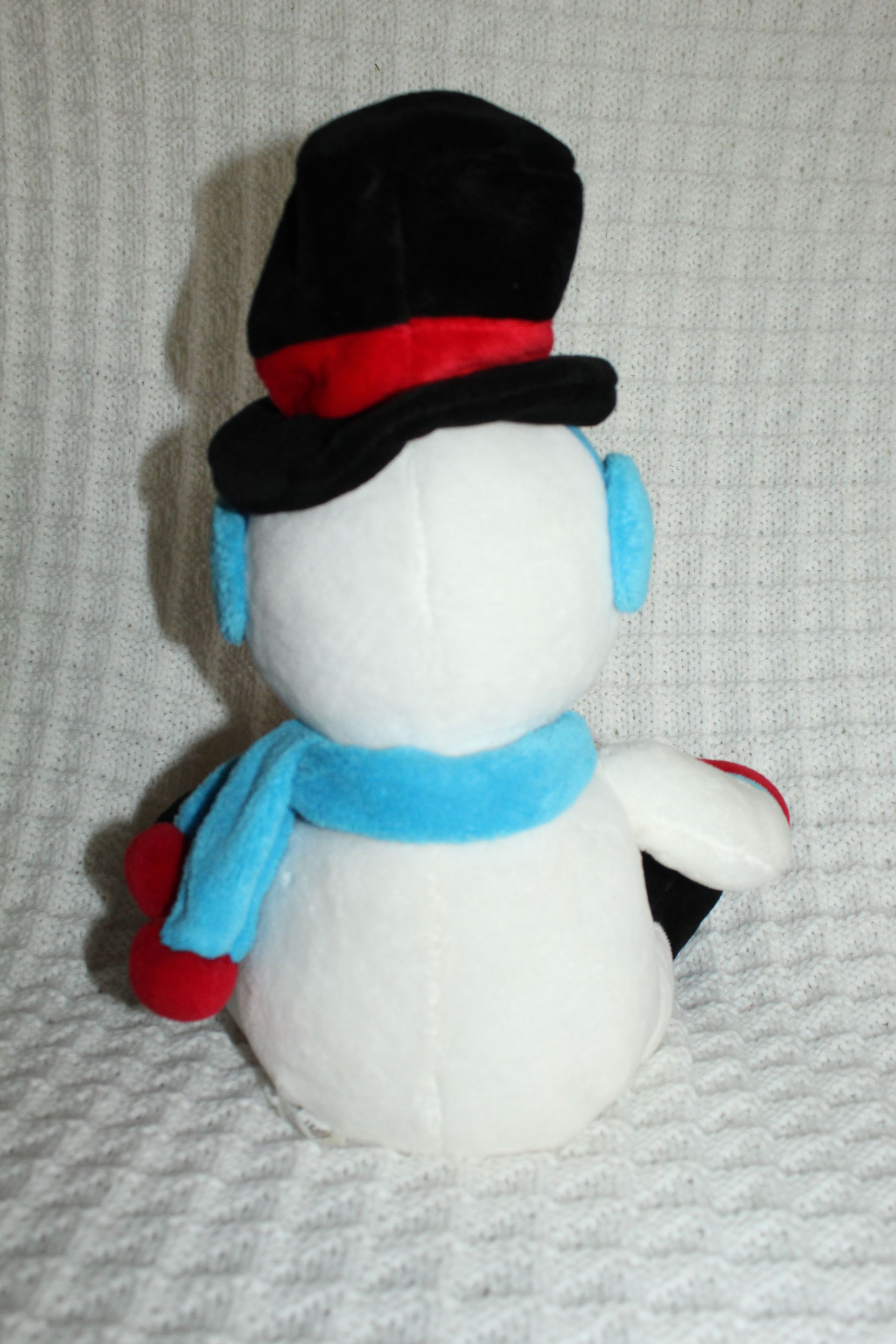 Snowman plush with black top hat, red accents, and a clear circular base on a textured white background