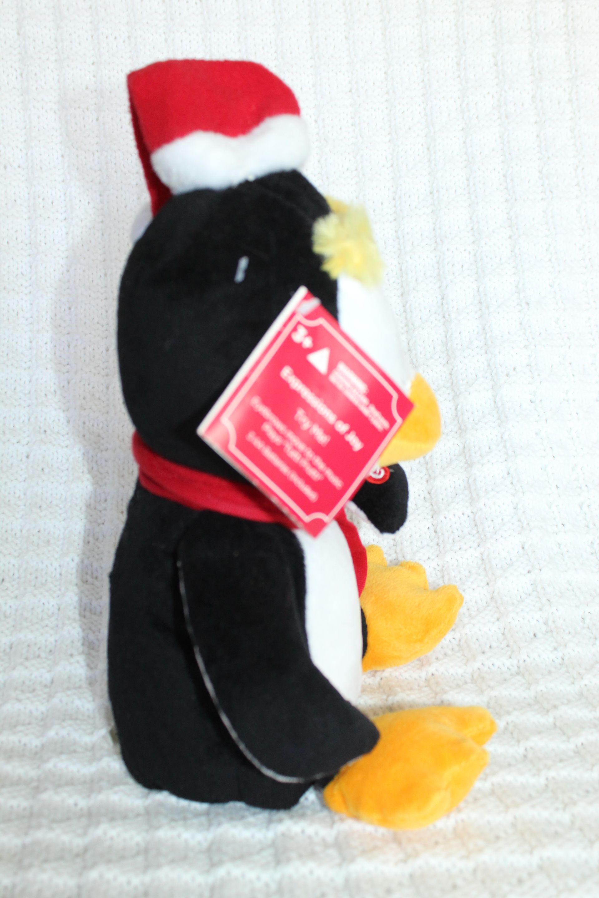 Black-and-white plush penguin wearing a red Santa hat and scarf, viewed from behind