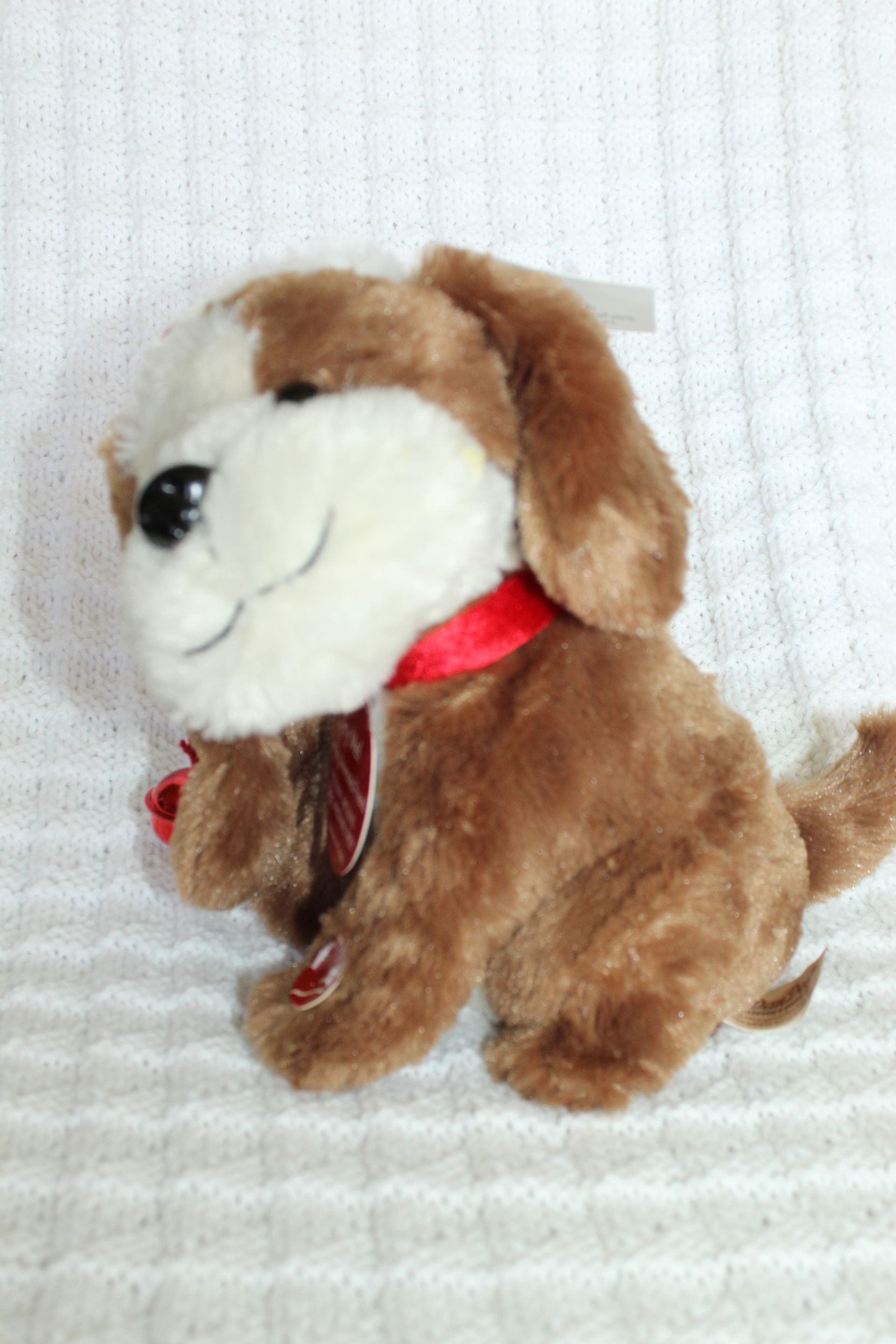 Small brown-and-white plush puppy wearing a red Santa hat and “Try Me” tag