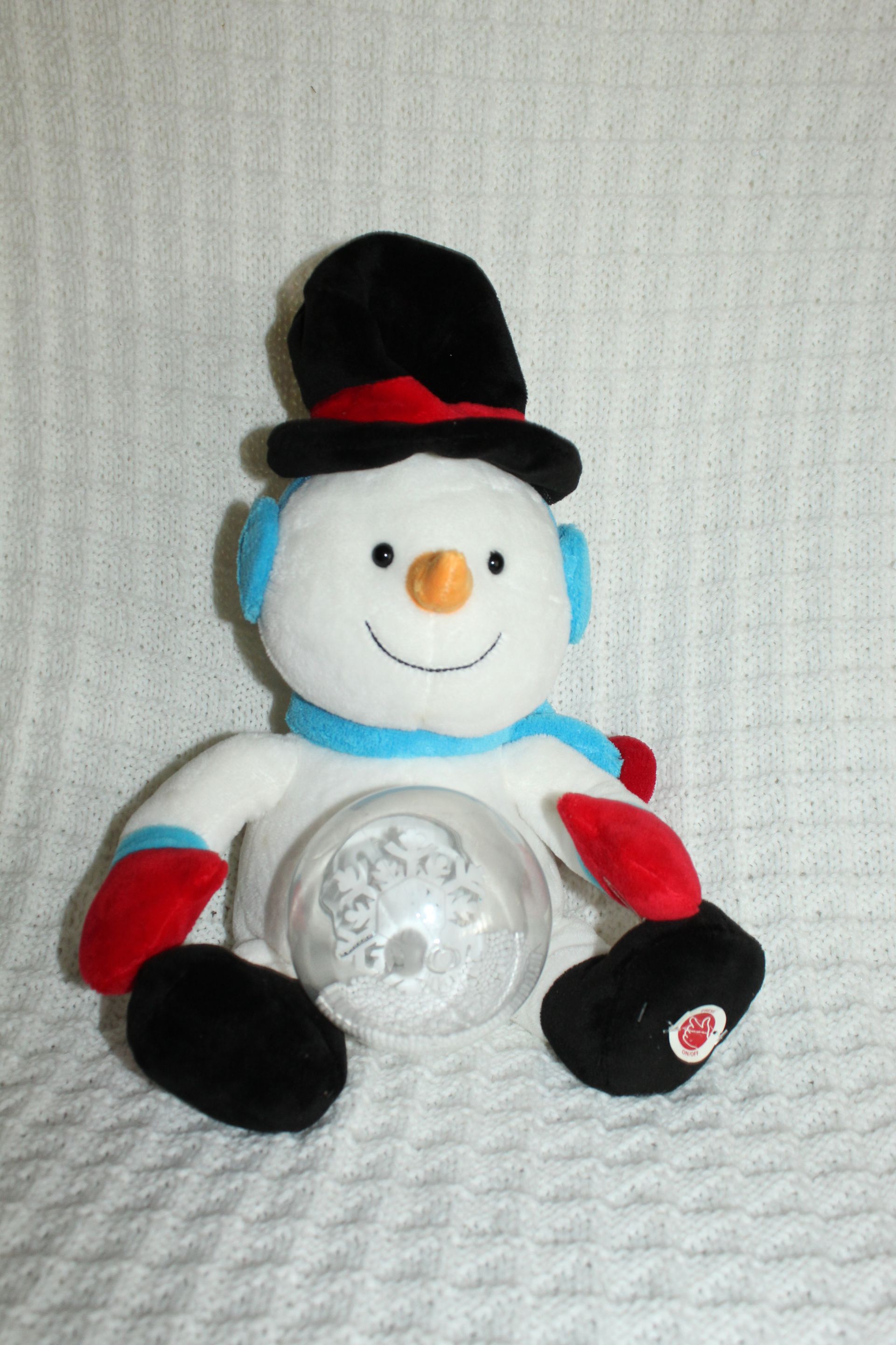 Snowman plush with black top hat, red accents, and a clear circular base on a textured white background