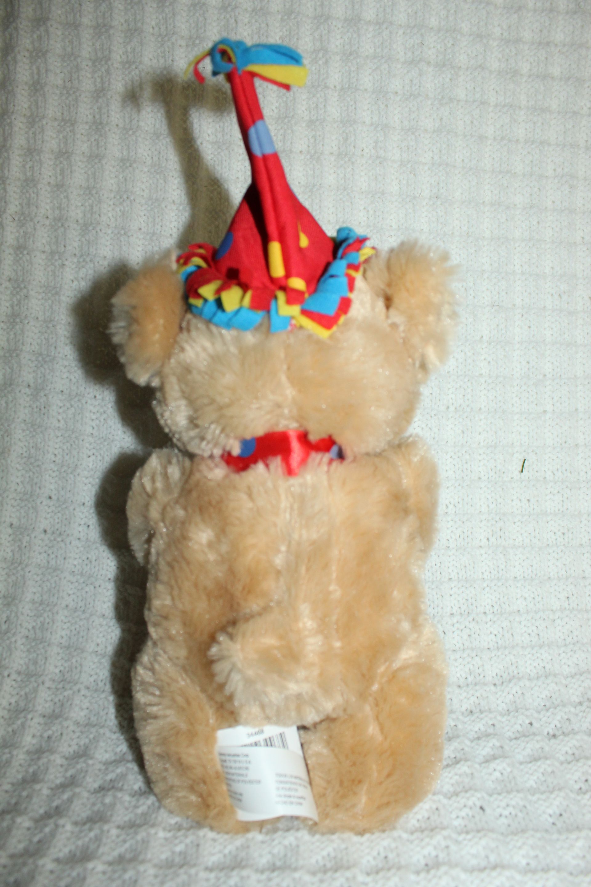 Tan plush toy with bright red and blue striped neck and a white tag, against a light textured background