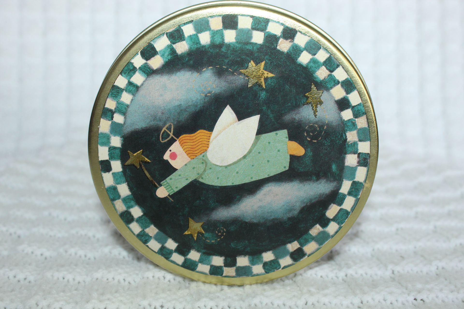 A sleeping angel on a round ornament with a green checkered border and dark cloudy background.