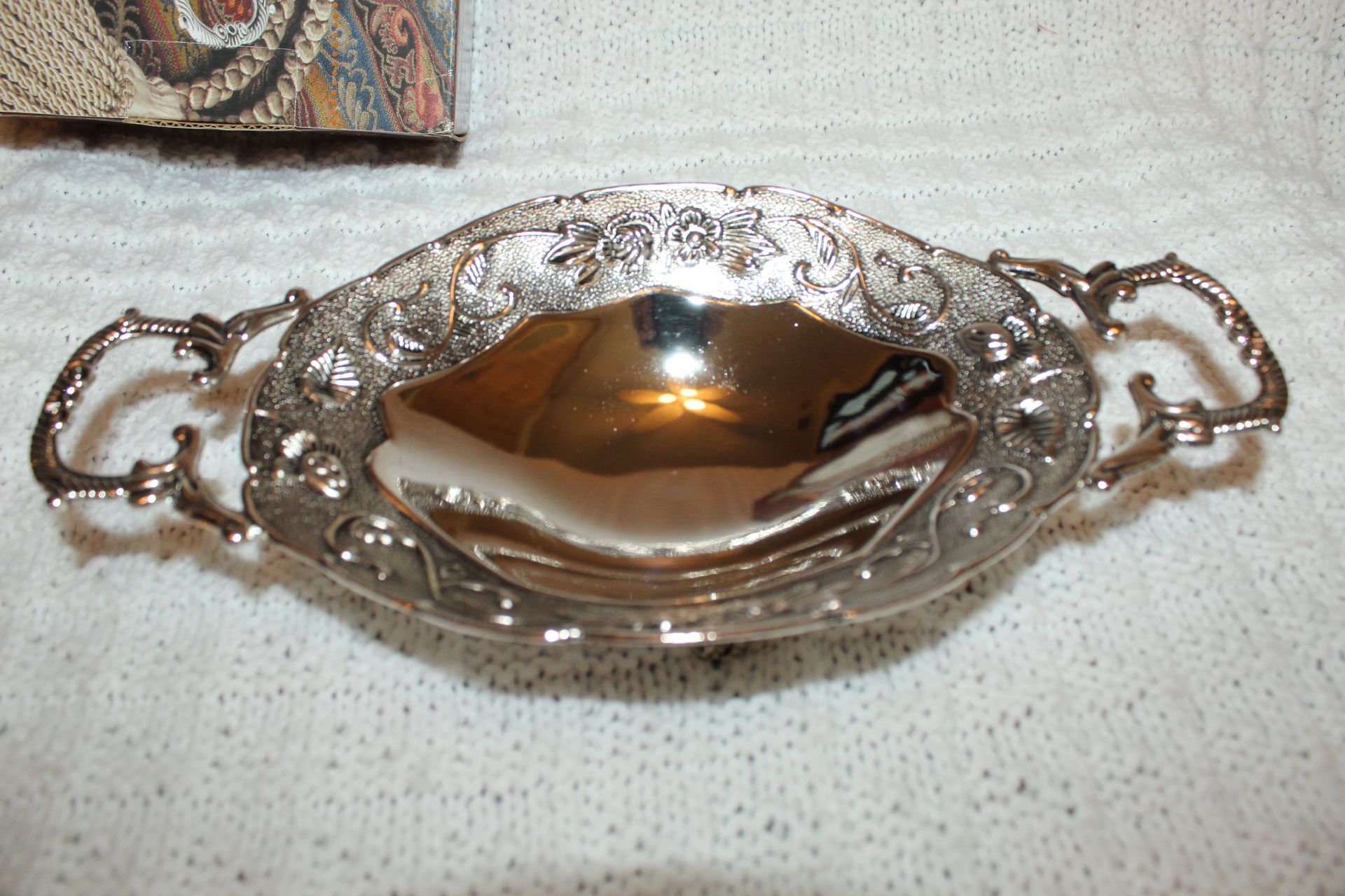 Ornate silver serving dish with decorative handles and a reflective gold-toned interior