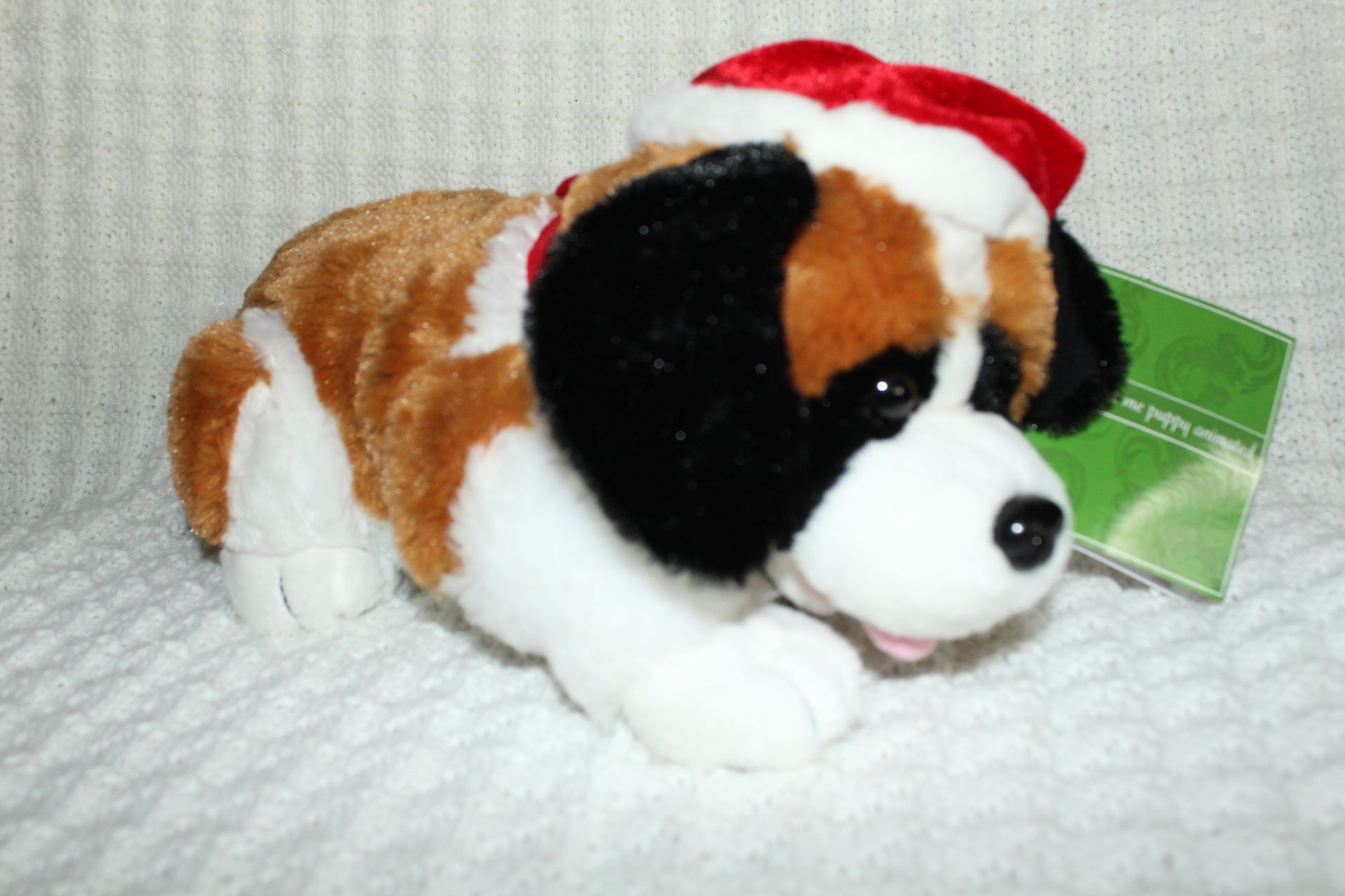 Plush St. Bernard puppy wearing a Santa hat on a white blanket