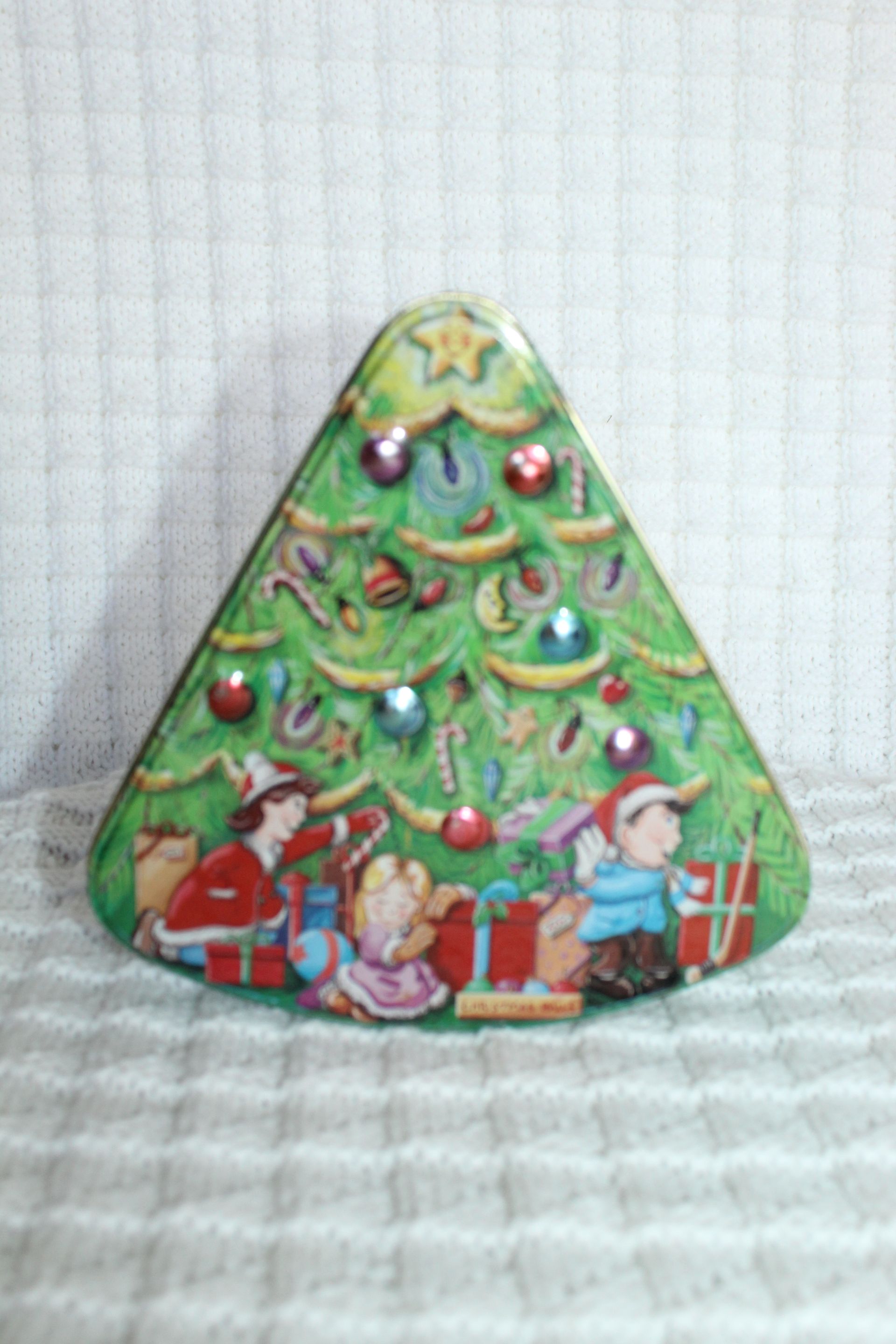 Christmas tree-shaped tin with colorful holiday scene and people decorating it