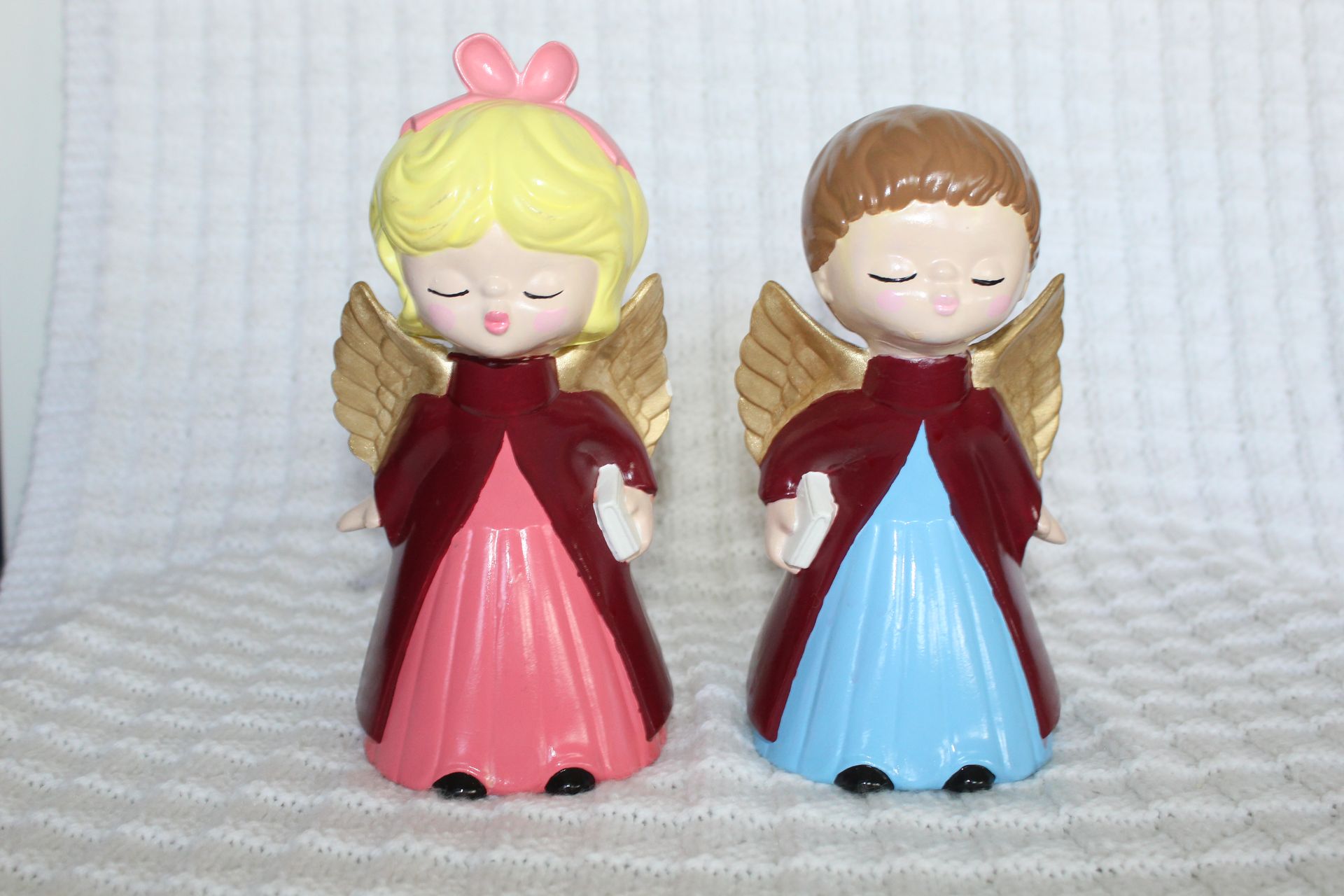 Two small figurines facing and touching noses, one blonde and one brown-haired, in red dresses.