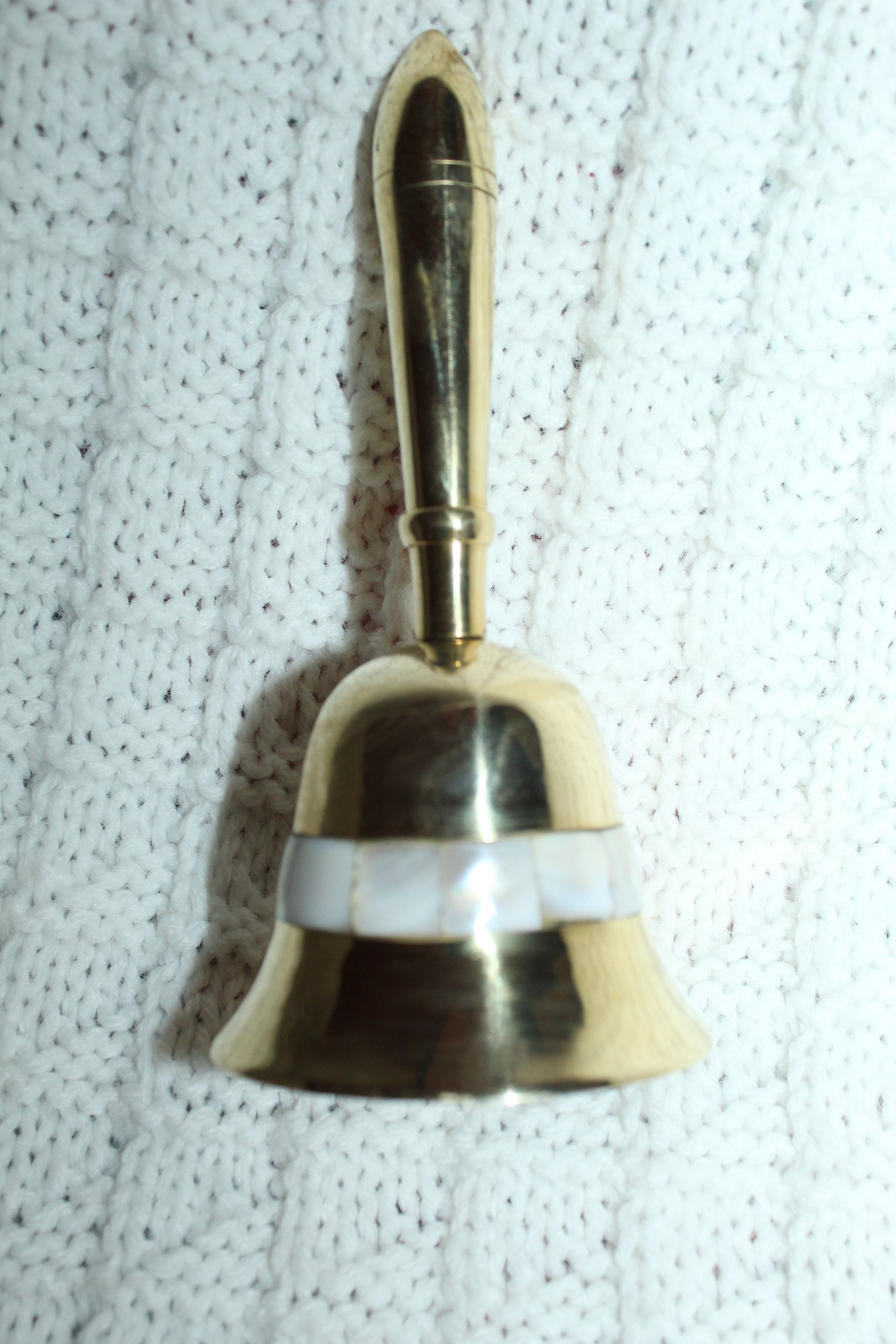 Brass bell with handle beside its red-and-black Brasseal box on a patterned cloth surface