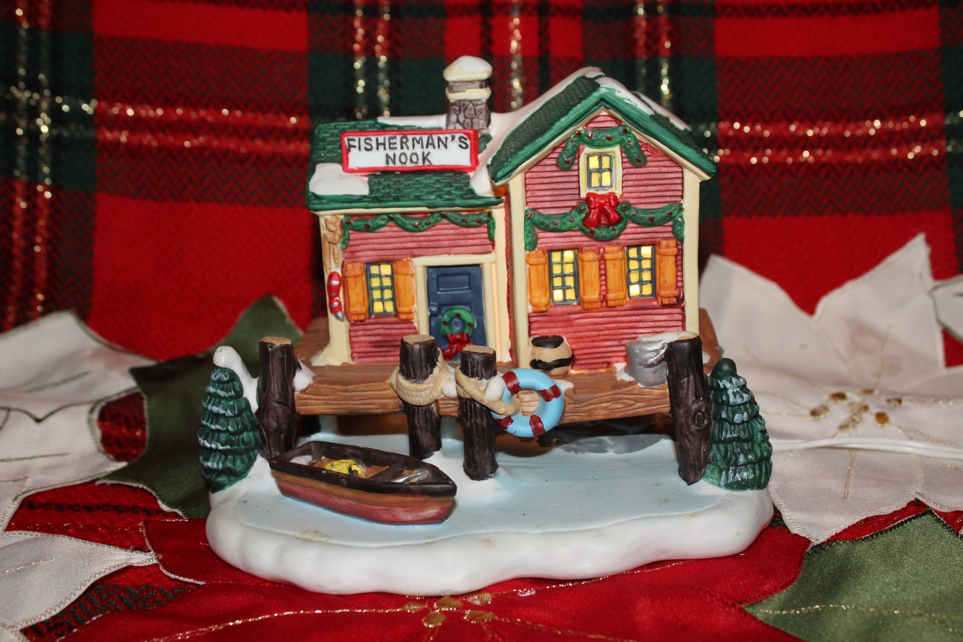 Miniature Christmas village house with figures, snow, and a red plaid holiday background