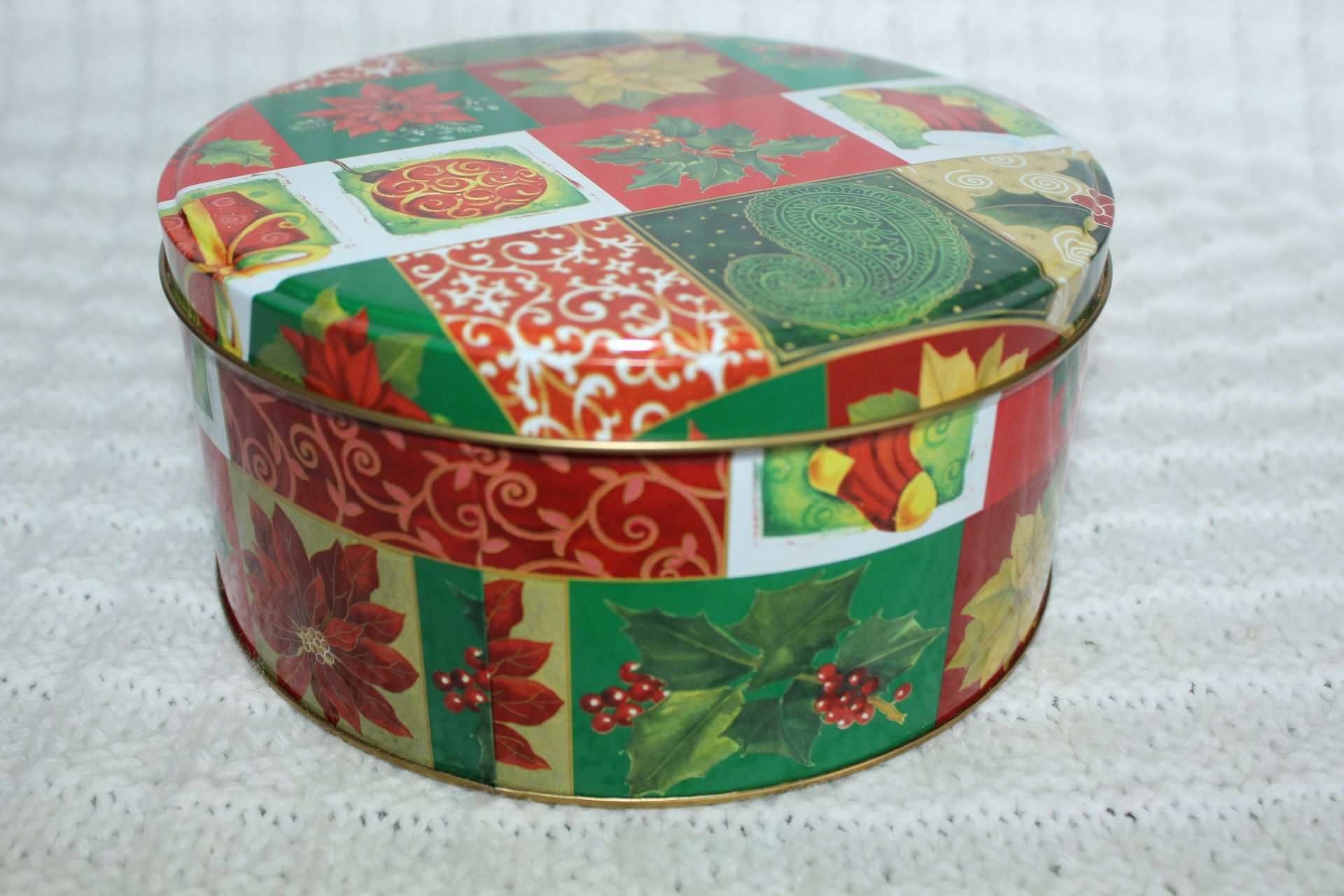 Festive red and green round gift tin with holiday patterns on a white textured surface