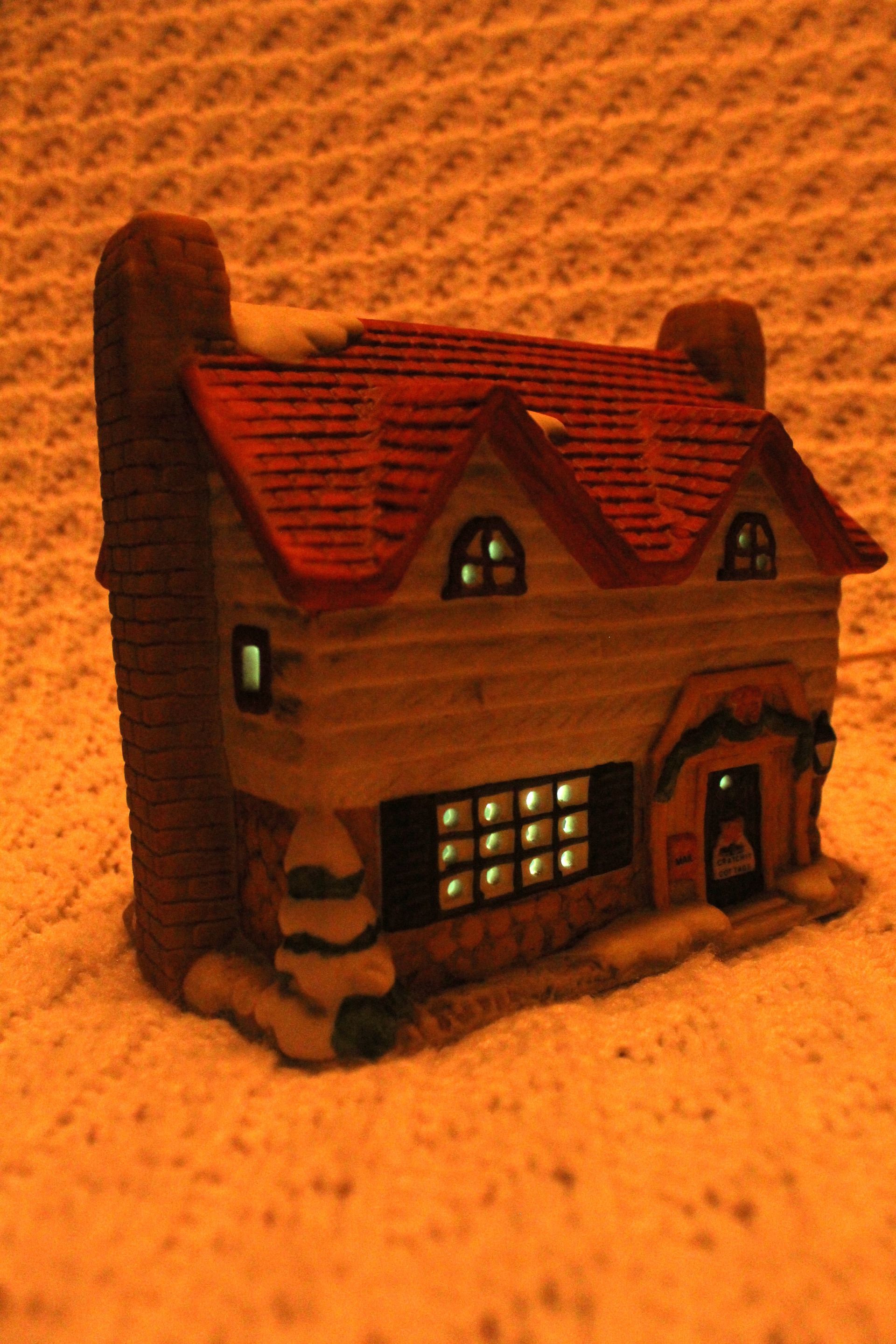 Small brown model house with lit windows on a textured orange surface