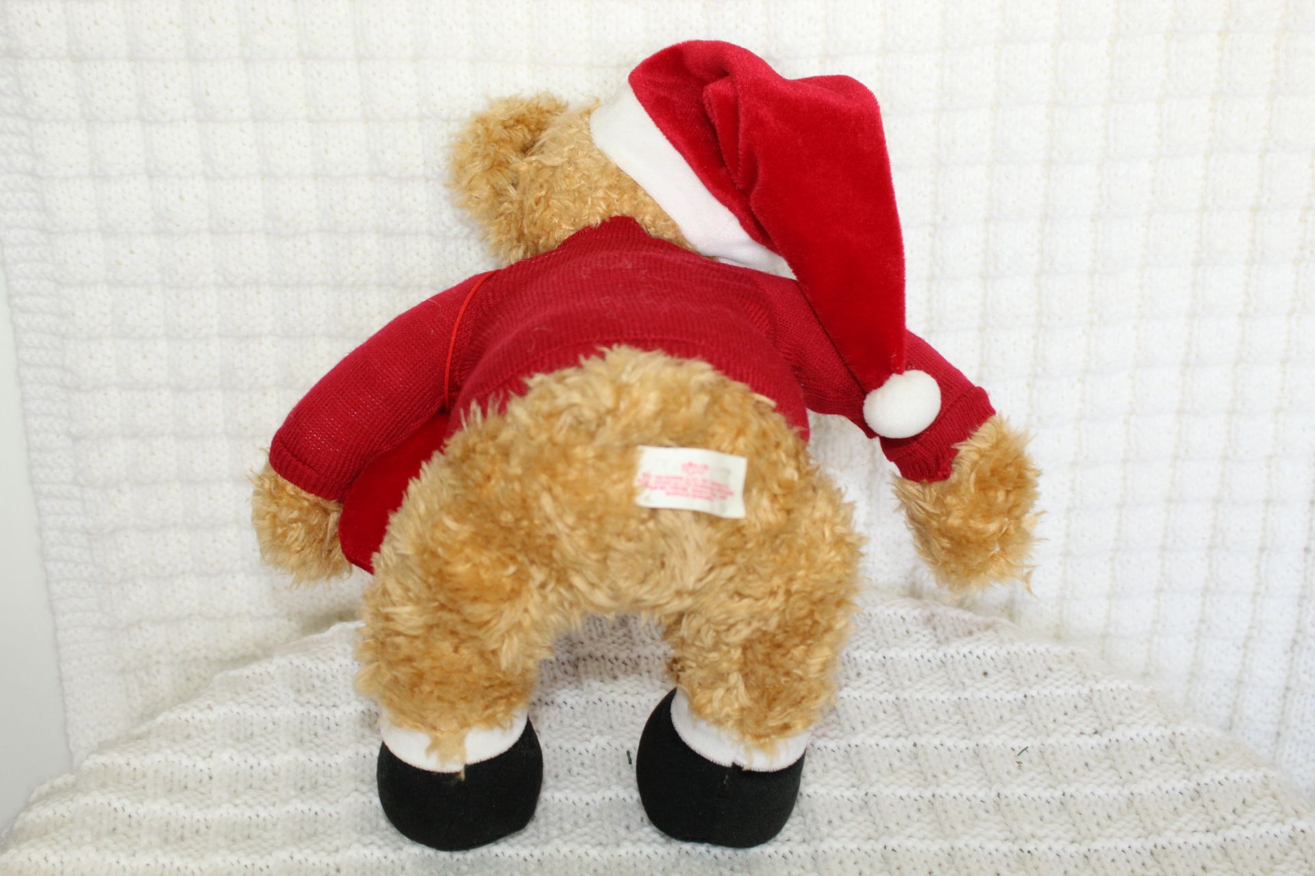 Teddy bear in a red Santa outfit with matching hat, sitting against a white background.