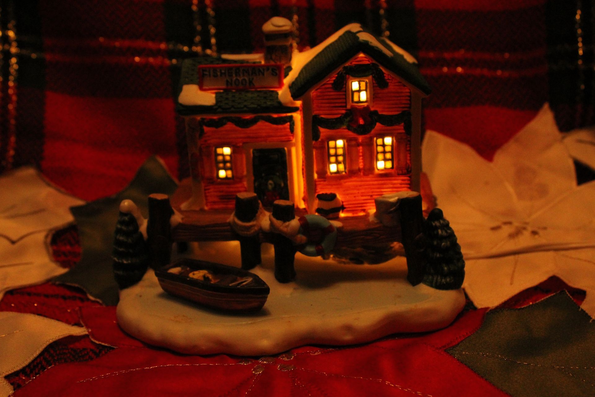 Miniature Christmas village house with figures, snow, and a red plaid holiday background