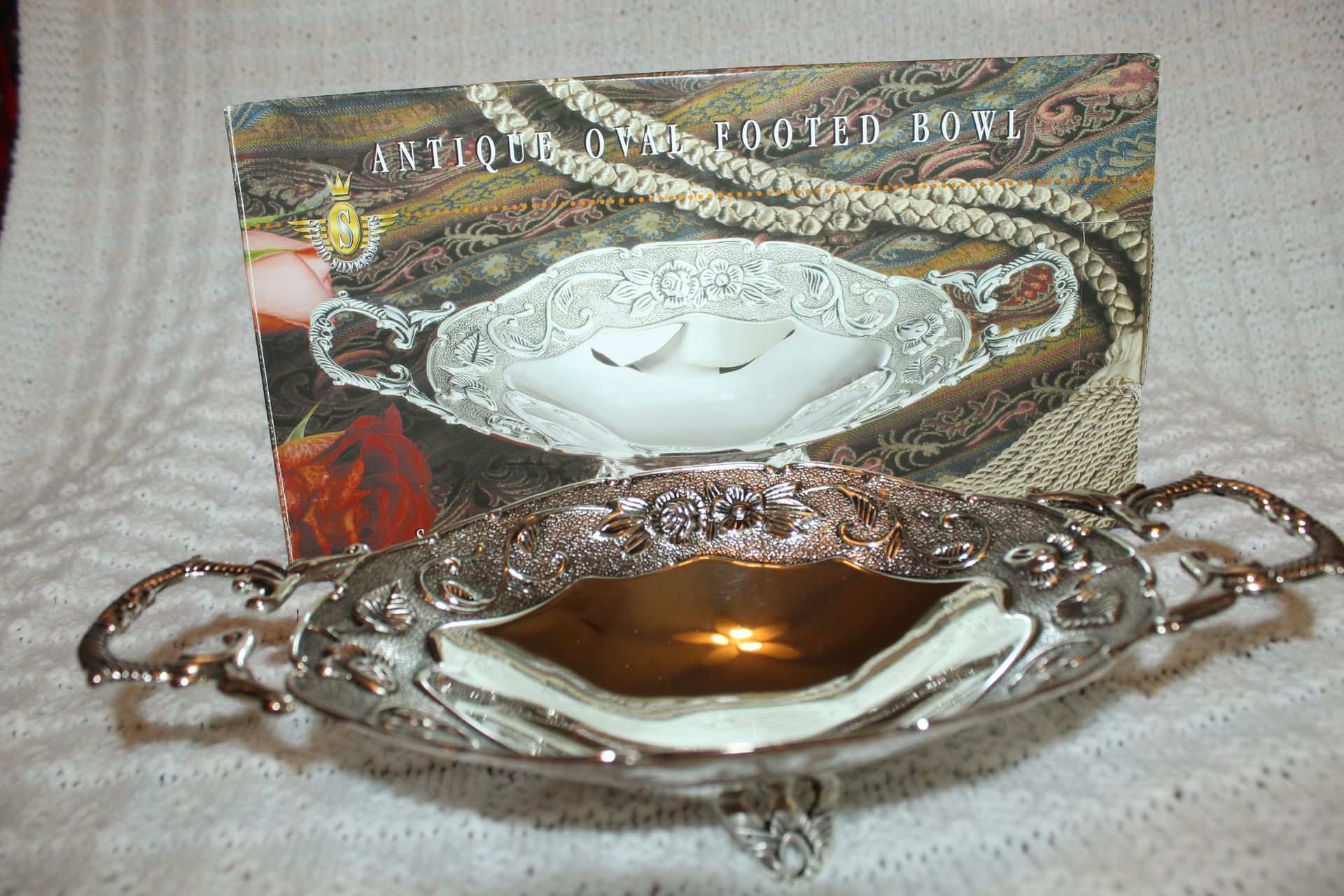 Ornate silver serving dish with decorative handles and a reflective gold-toned interior