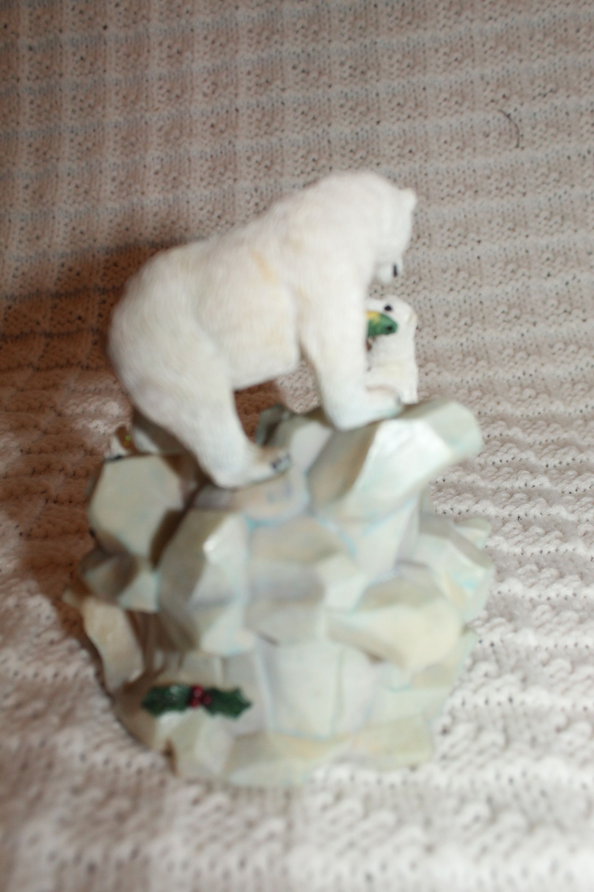 Small white bear figurine on a rocky base, reaching toward a smaller bear amid green foliage.