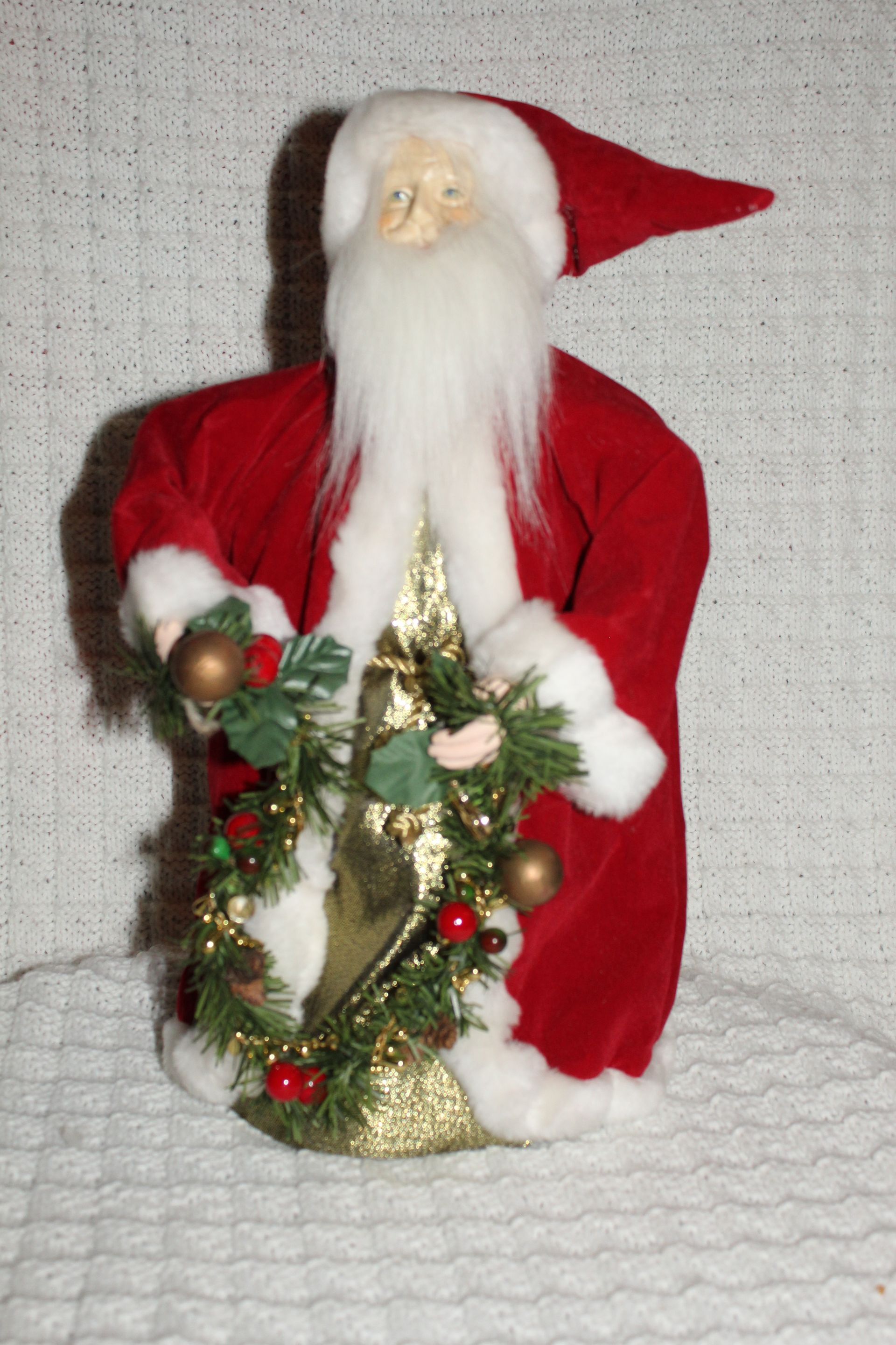 Santa figurine in red suit holding a decorated Christmas tree and wreath in a gold sack