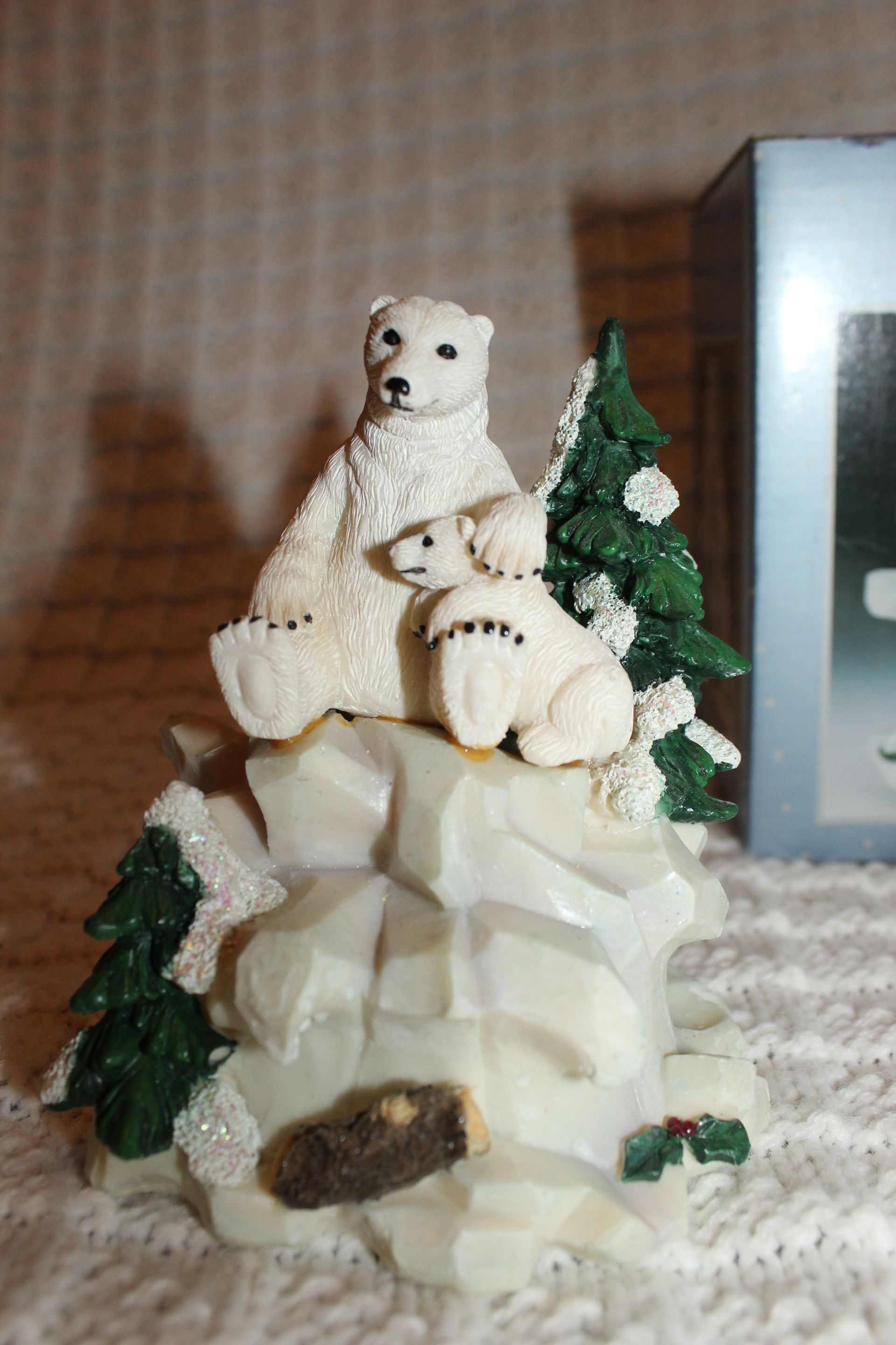 Polar bear figurines on a snowy rock with evergreen trees and a small cave opening