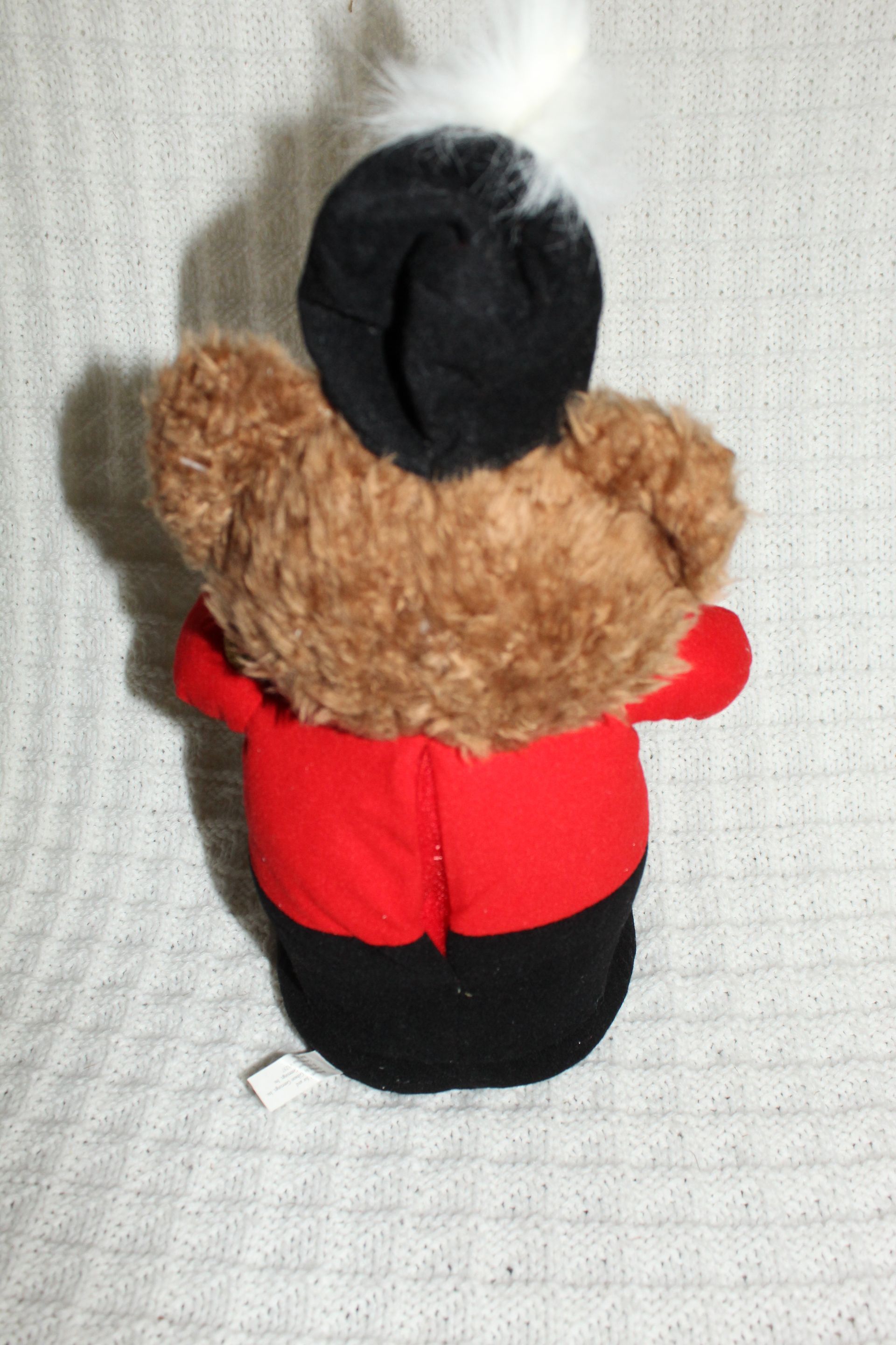 Brown teddy bear in red outfit holding a drum, with a black-and-white feathered hat