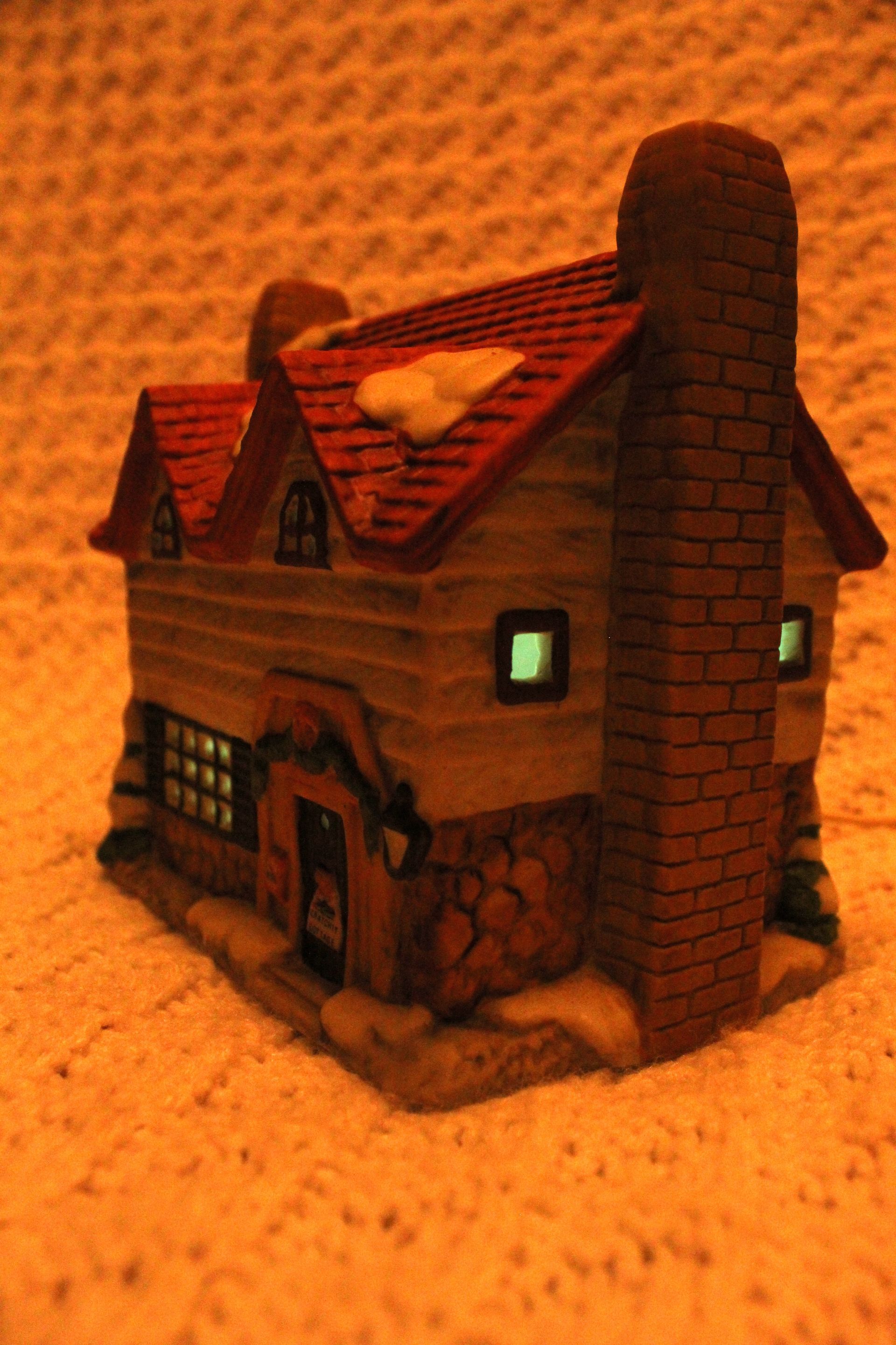 Small brown model house with lit windows on a textured orange surface