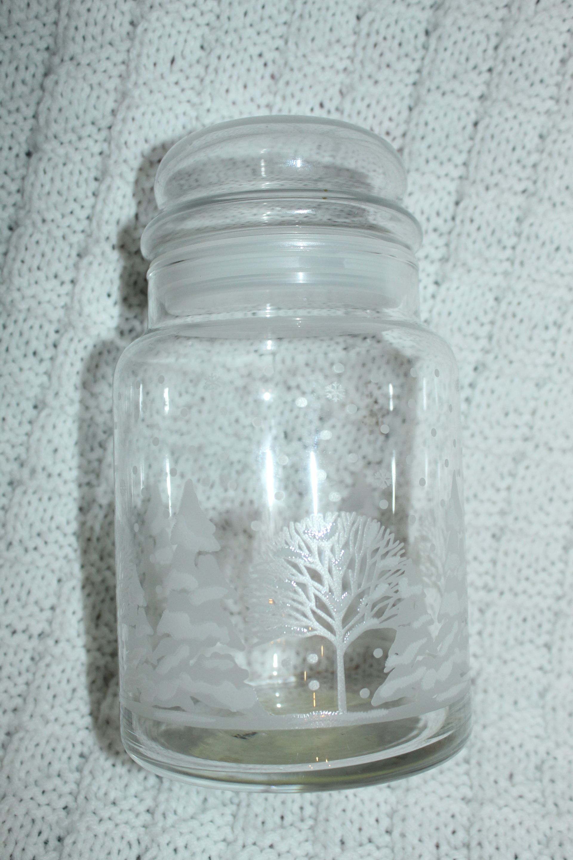 Clear glass jar with etched floral design on a textured white fabric background