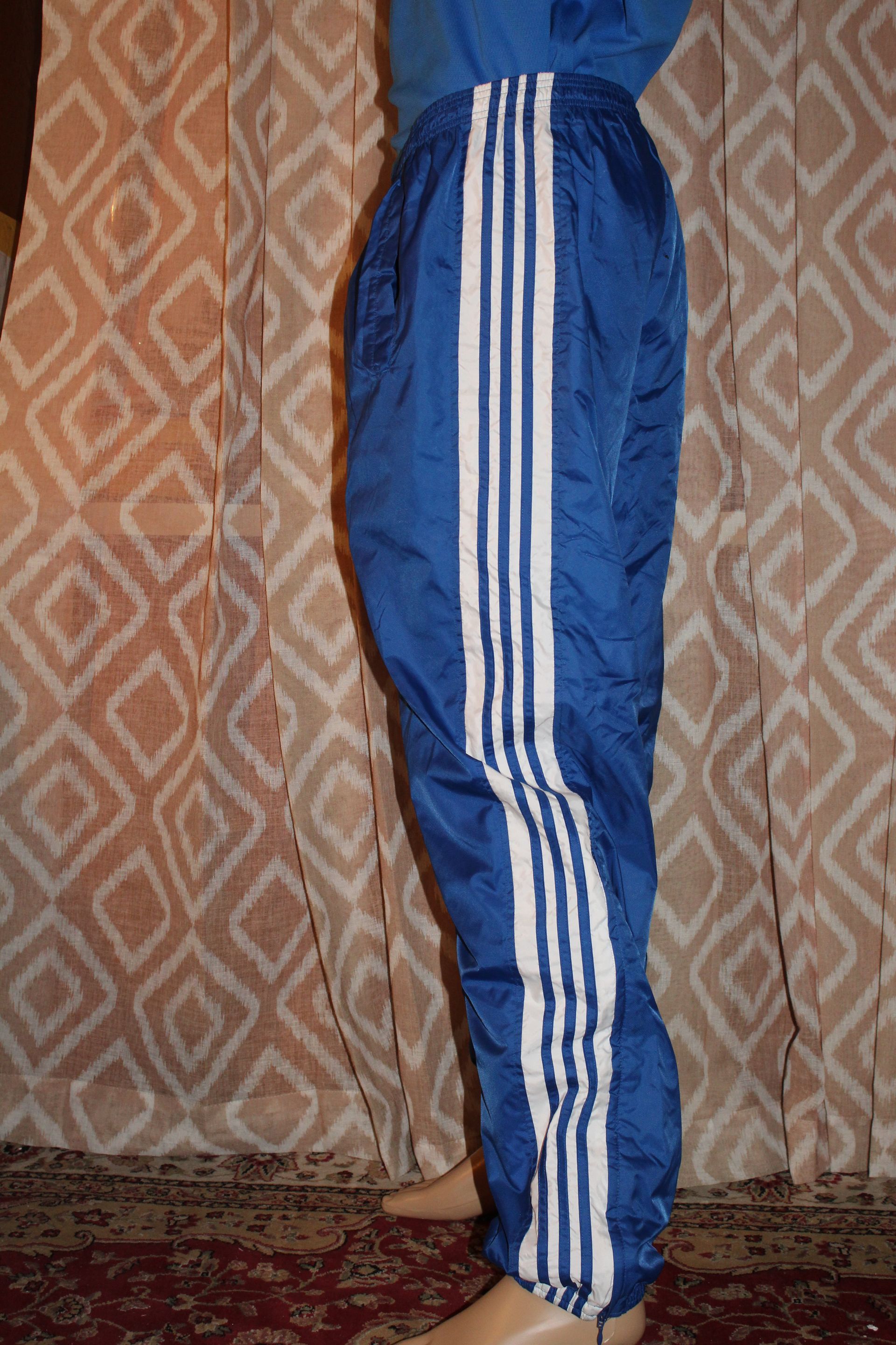 Person wearing blue athletic pants standing indoors against a patterned curtain.