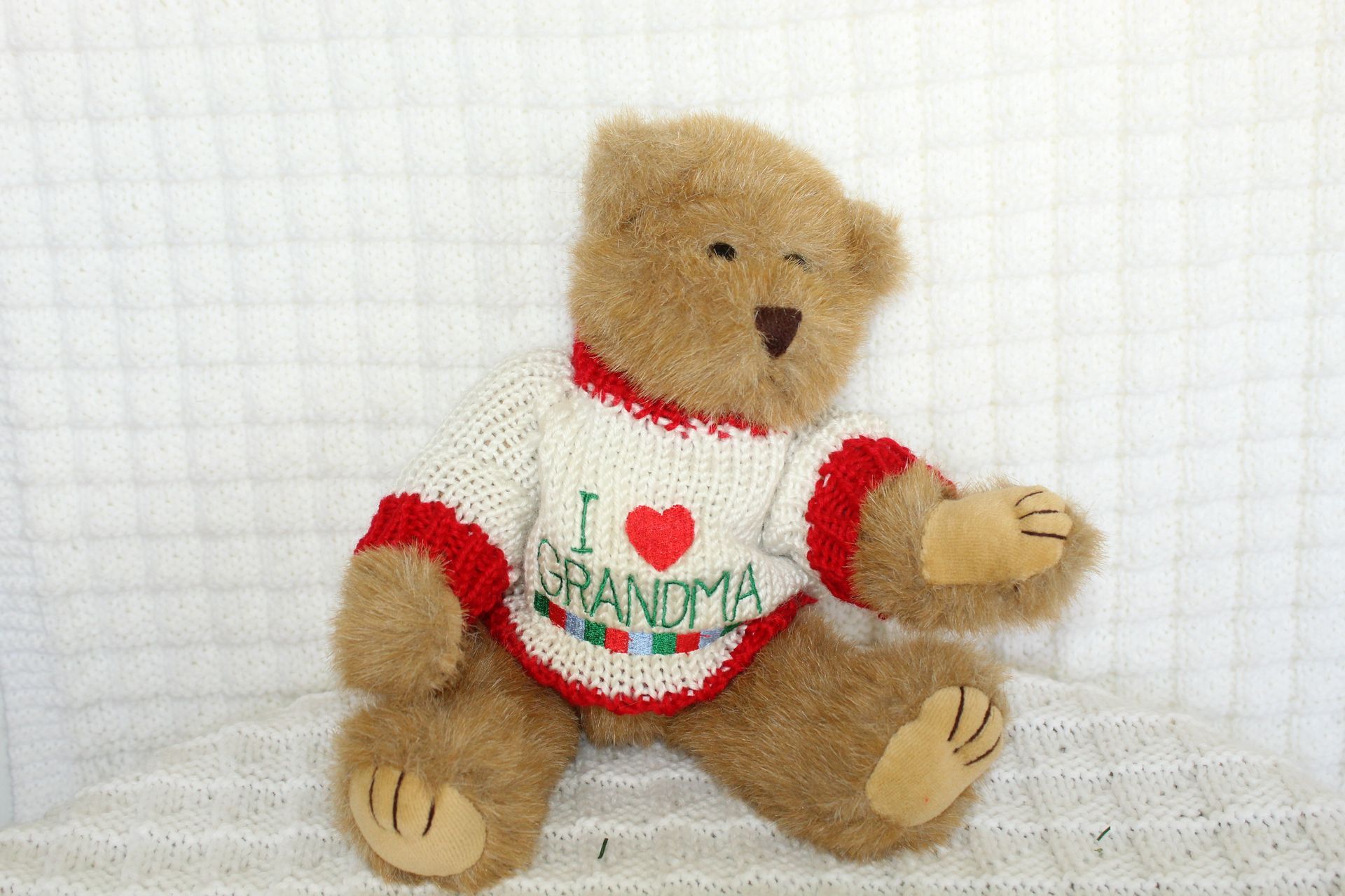 Small teddy bear in a white shirt with red trim and “Grandma” text, sitting on a white textured surface.