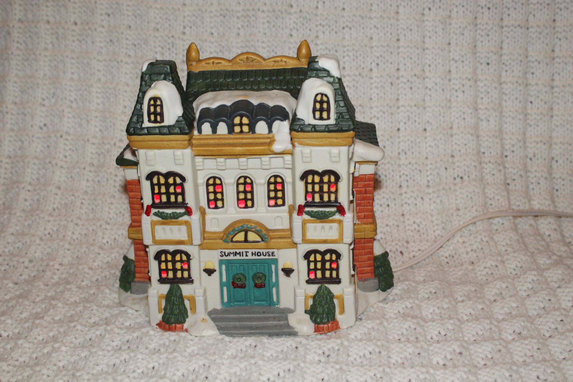 Colorful miniature dollhouse with a teal front door and white facade on a textured cloth background