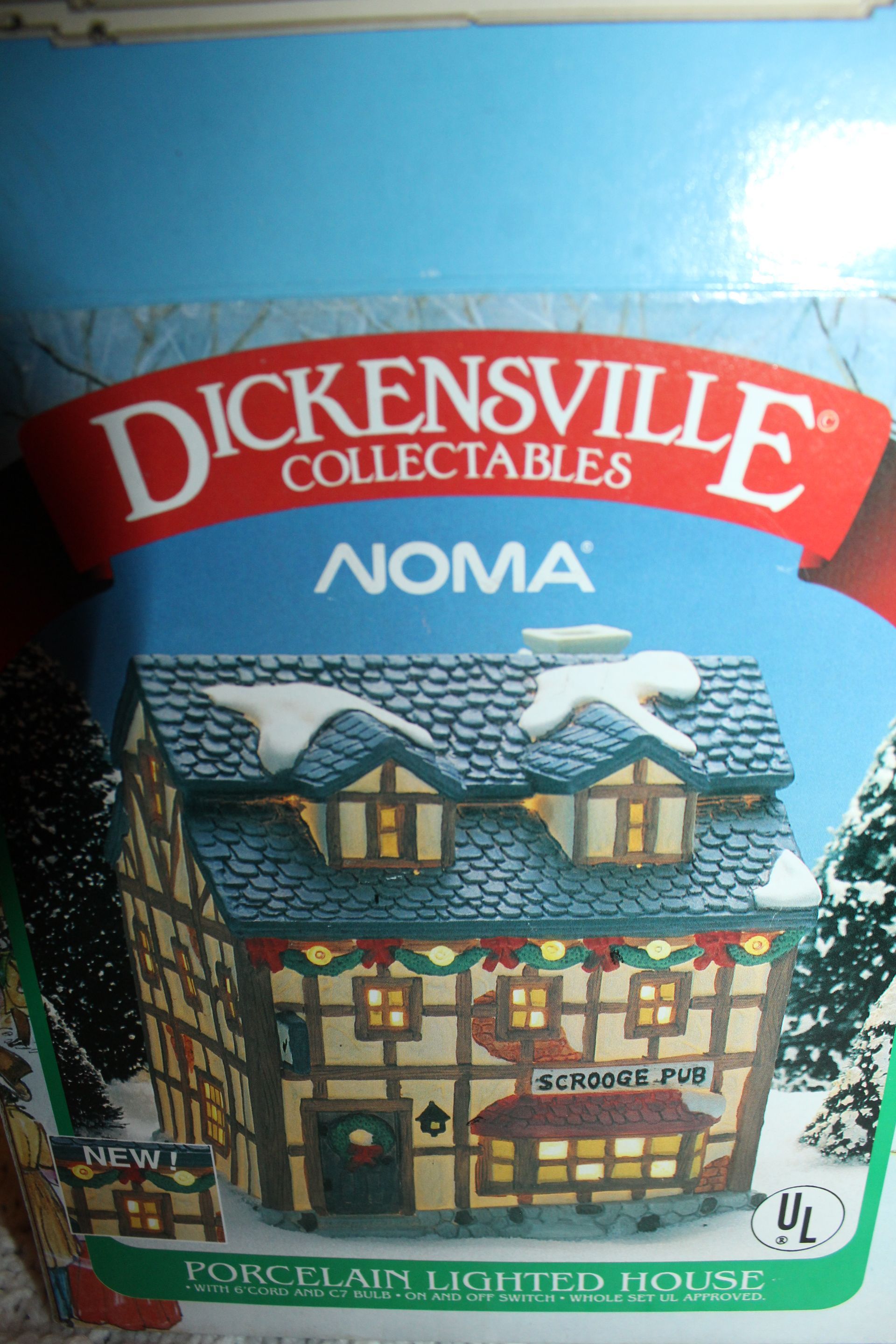 Dickensville Collectables Noma ceramic cottage in a blue box with red logo and snowy roof display.