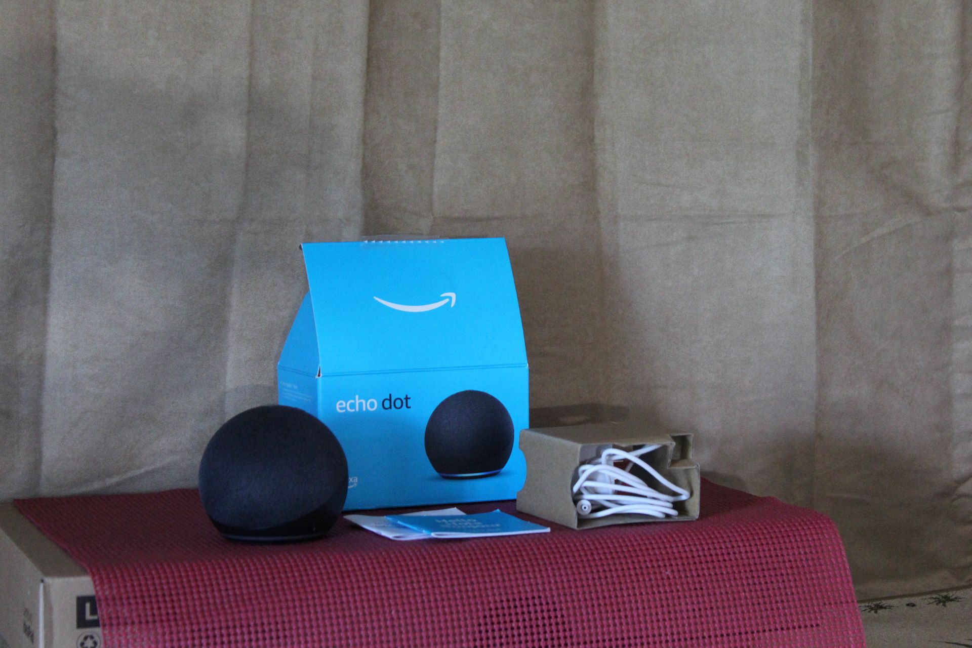 Blue box with two black spheres and a small white item on a red cloth against a gray couch.