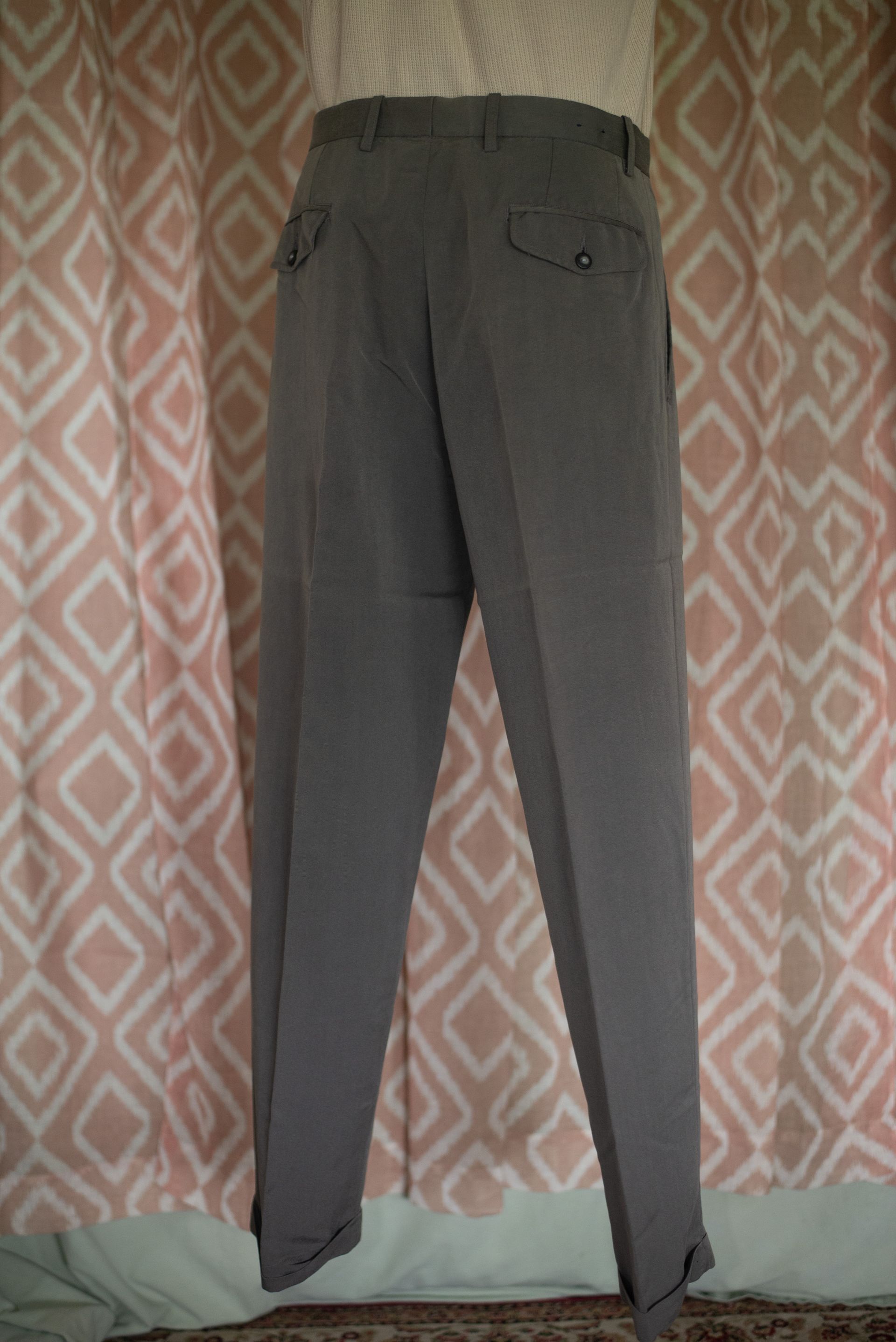 Gray pants hanging against a patterned curtain.