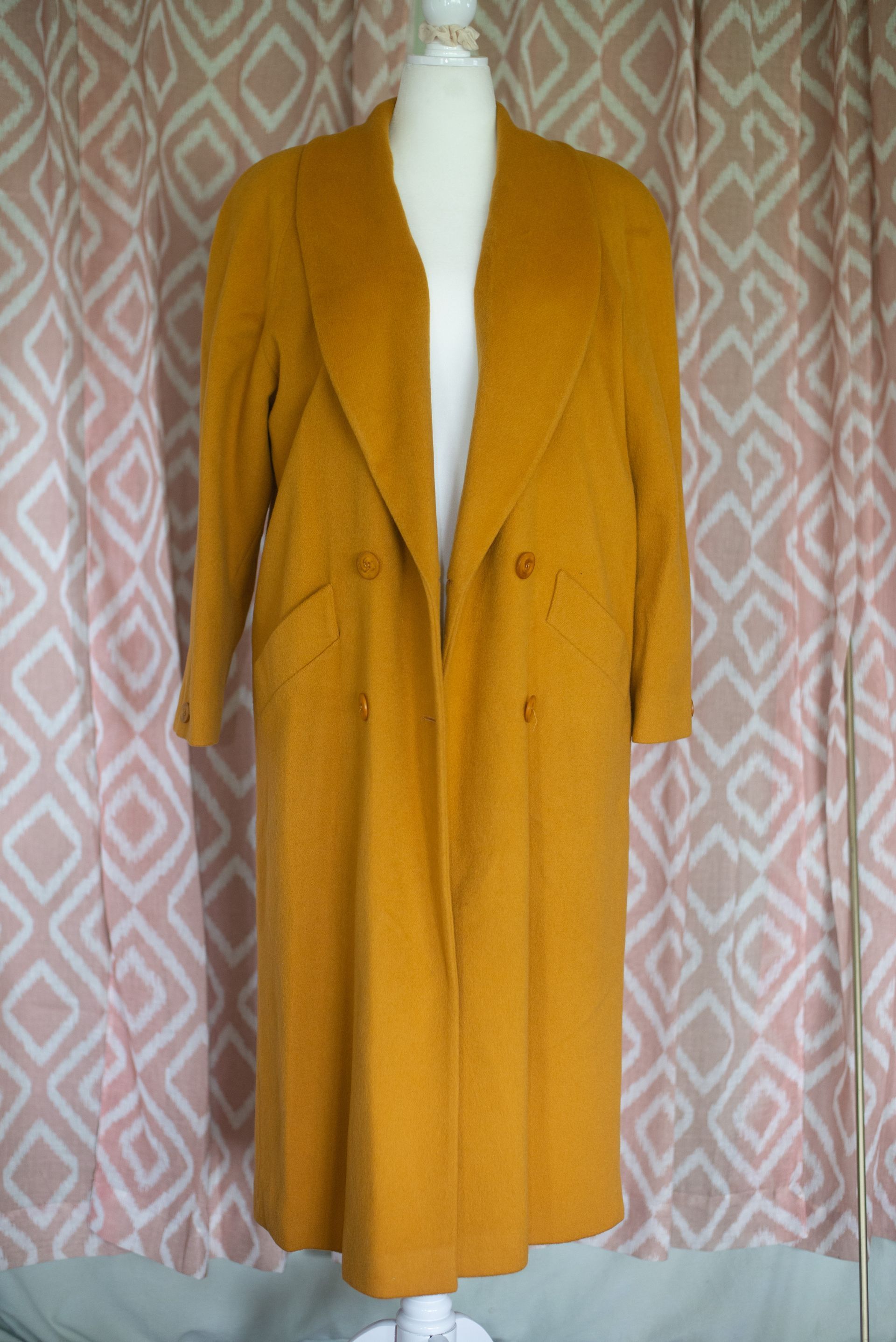 Mustard yellow long coat on a mannequin against a patterned curtain.