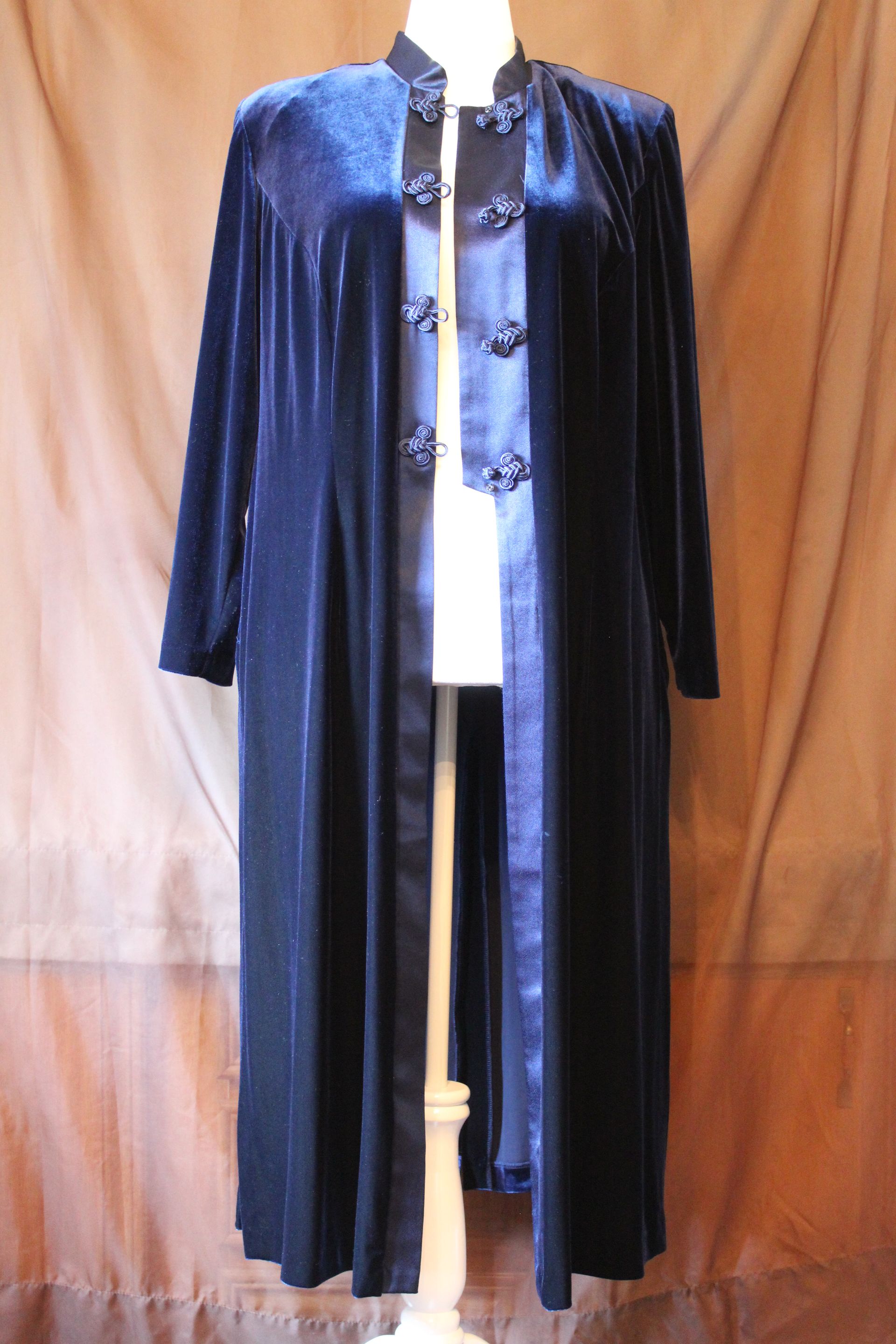 Blue long coat with black trim displayed on a mannequin against a tan curtain background