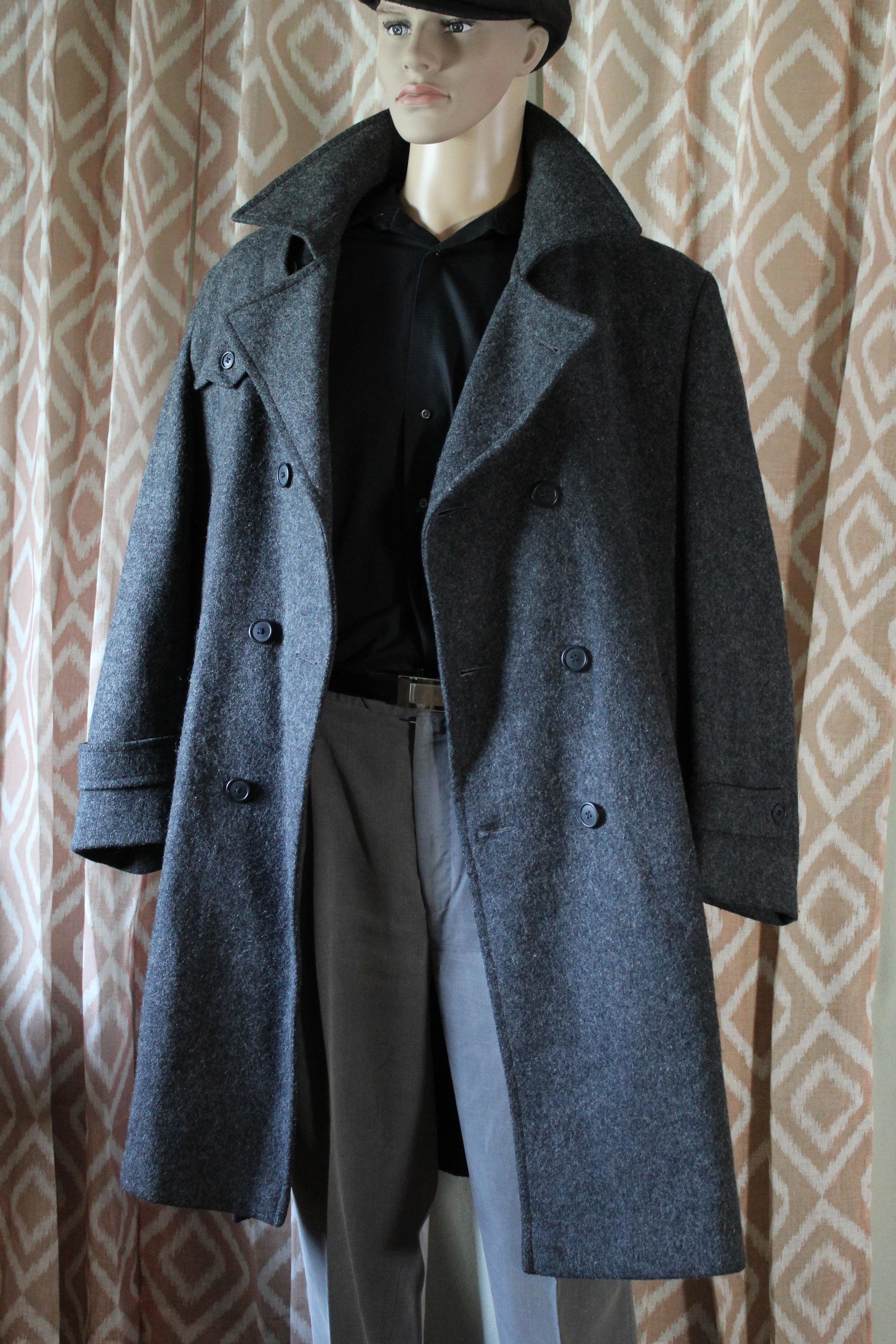 Mannequin wearing a dark gray overcoat, black top, and gray trousers against a patterned curtain