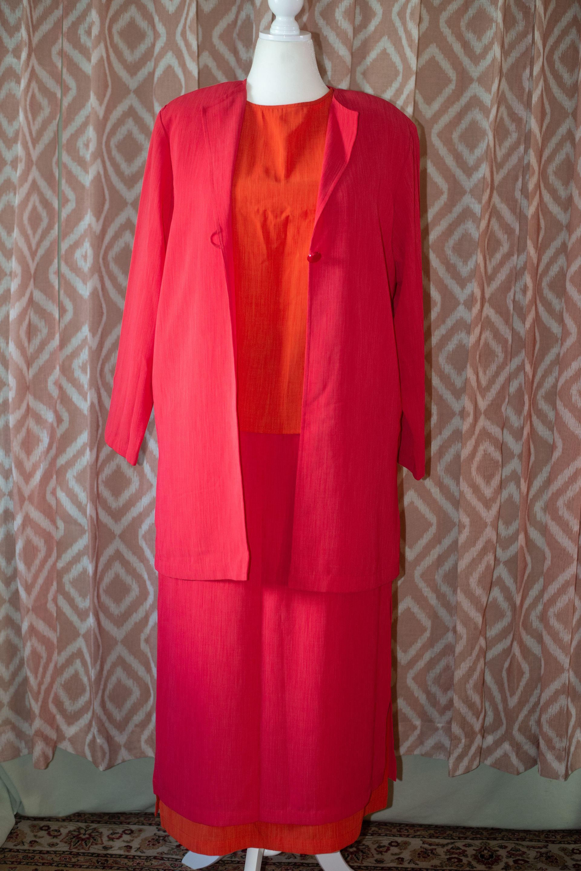 Pink jacket and matching skirt displayed on a mannequin against a patterned backdrop