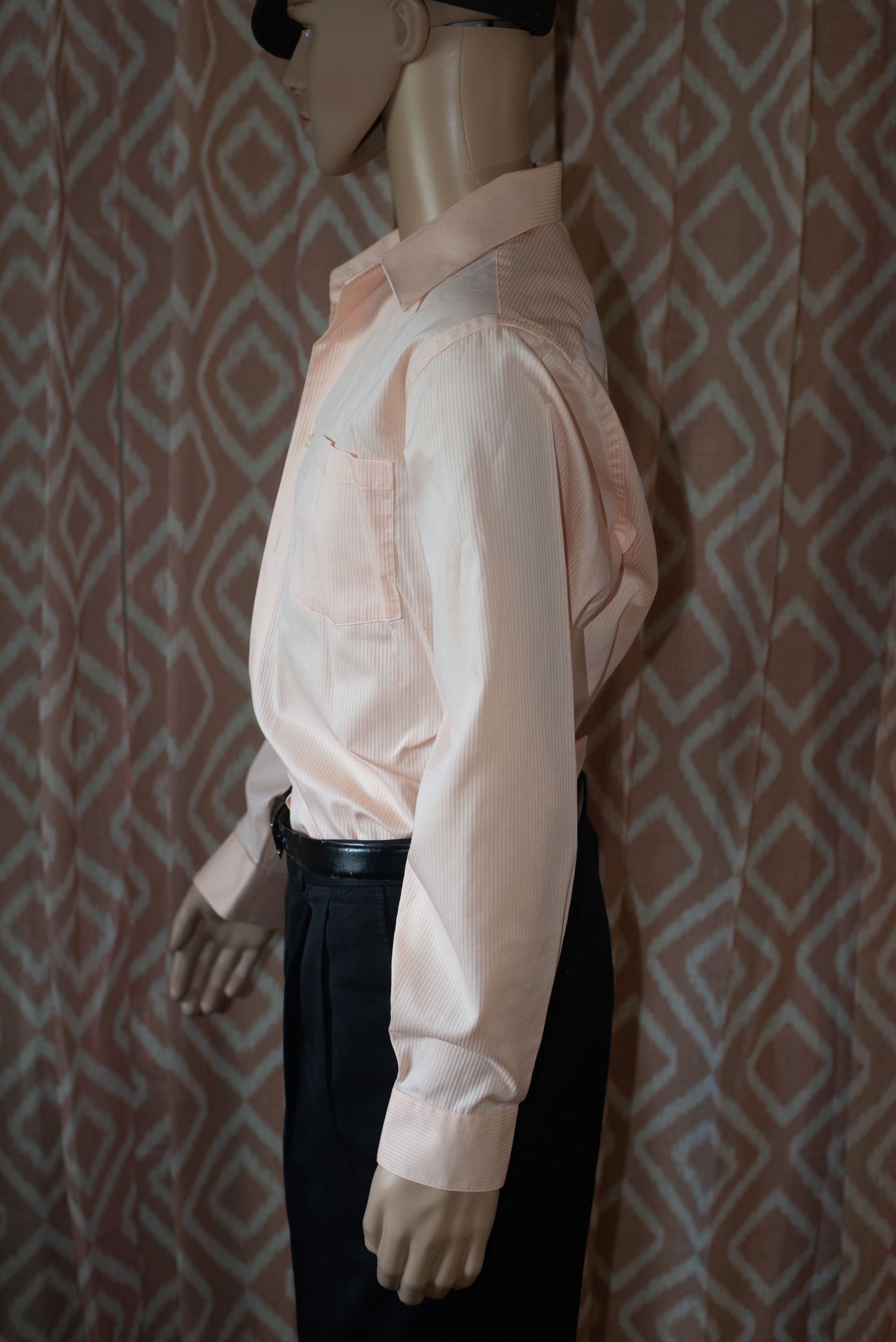 Mannequin wearing a pale pink button-up shirt and black pants against a patterned wallpaper background