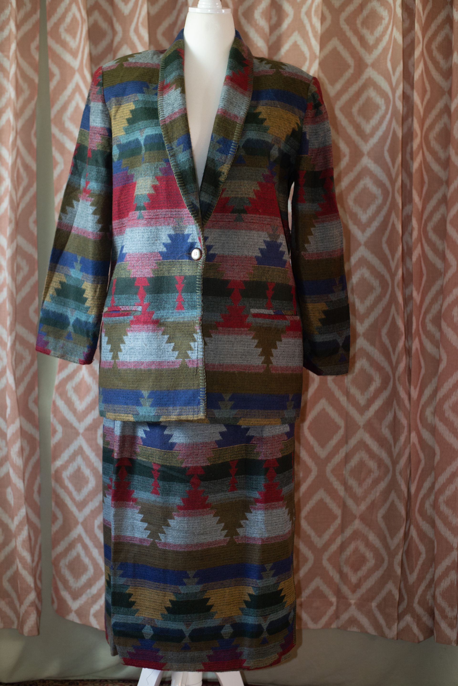 Colorful patterned blazer and skirt set displayed on a mannequin in front of curtains