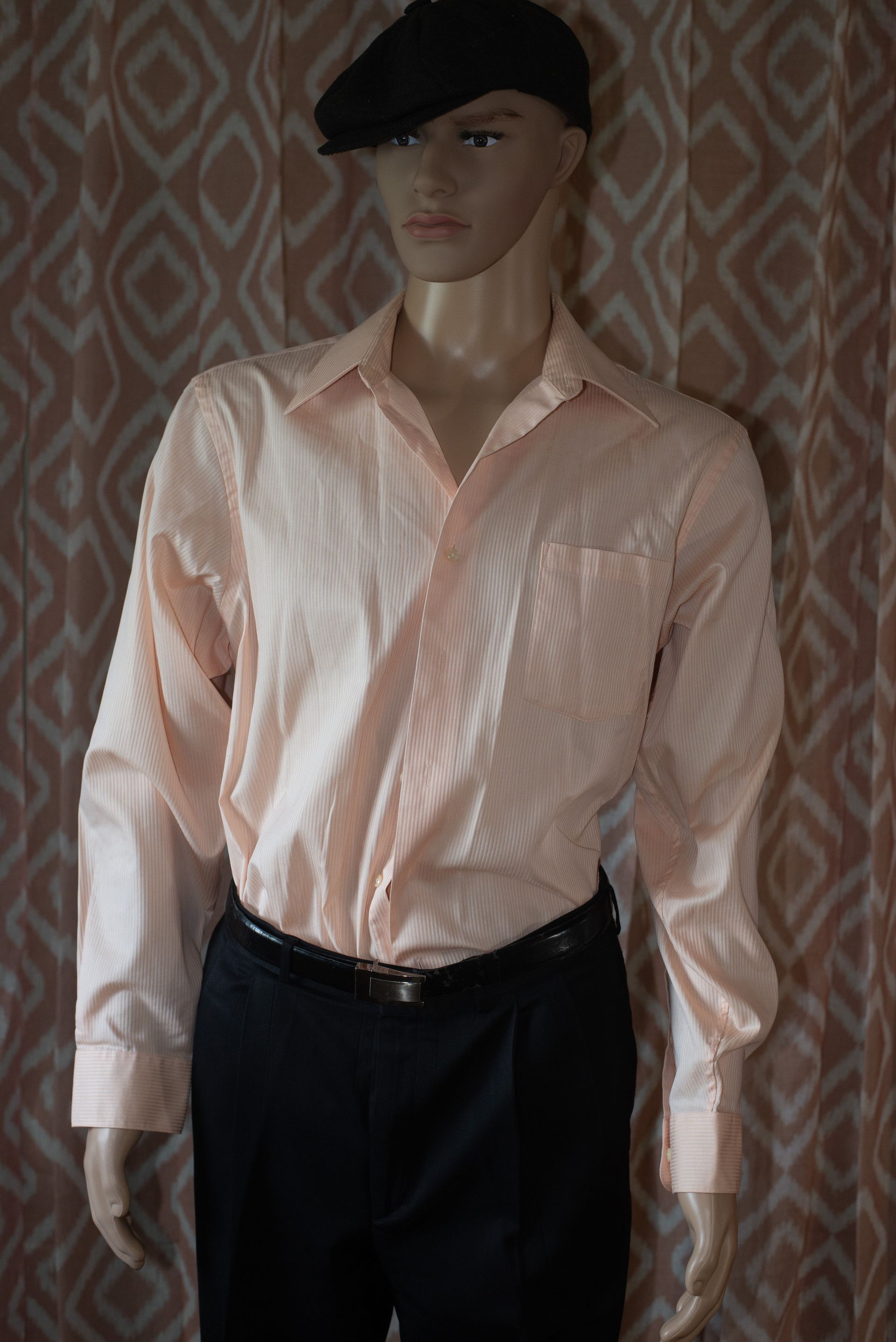 Mannequin wearing a pale pink button-up shirt and black pants against a patterned wallpaper background