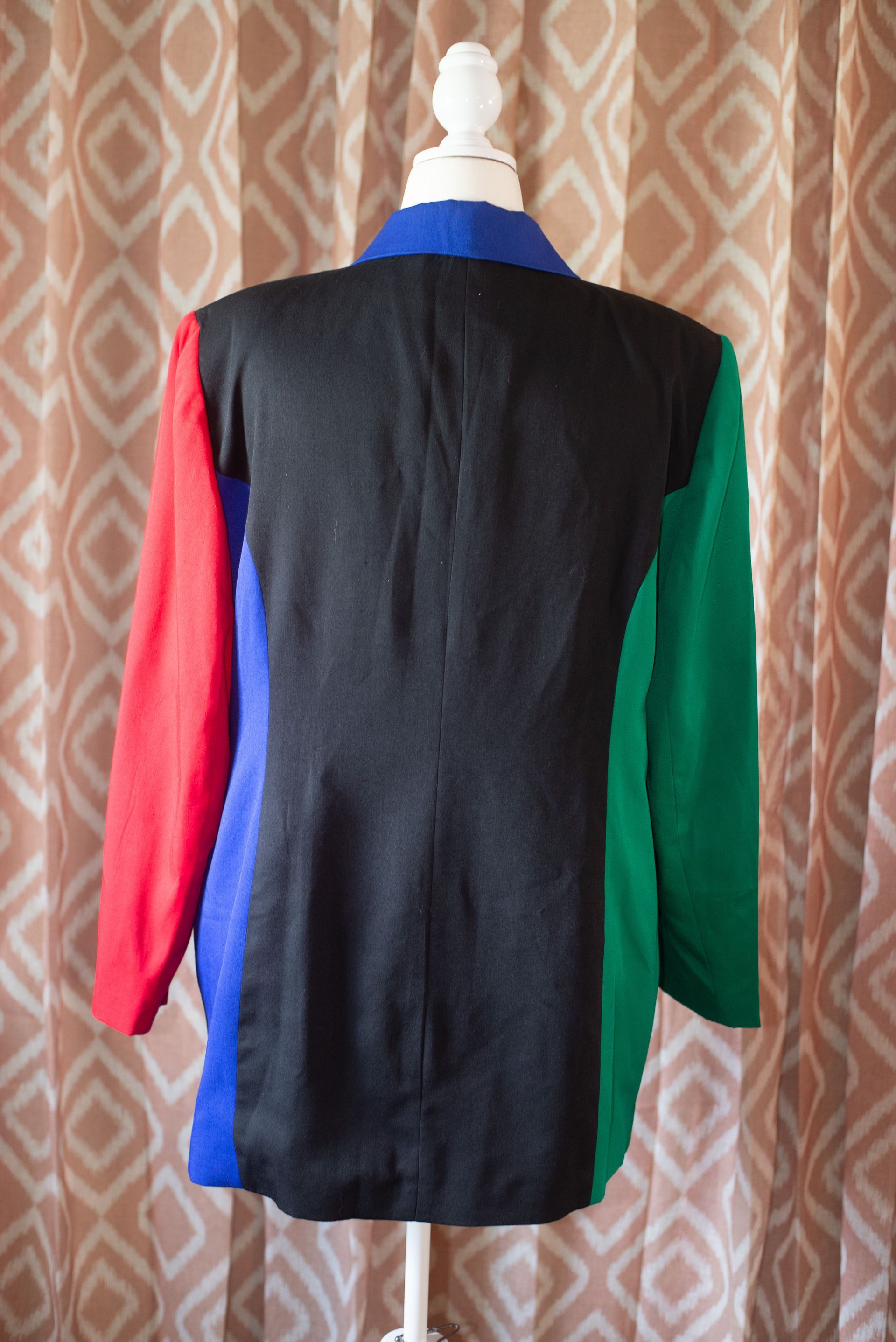 Colorful patchwork jacket with red sleeves on a mannequin against a patterned curtain background