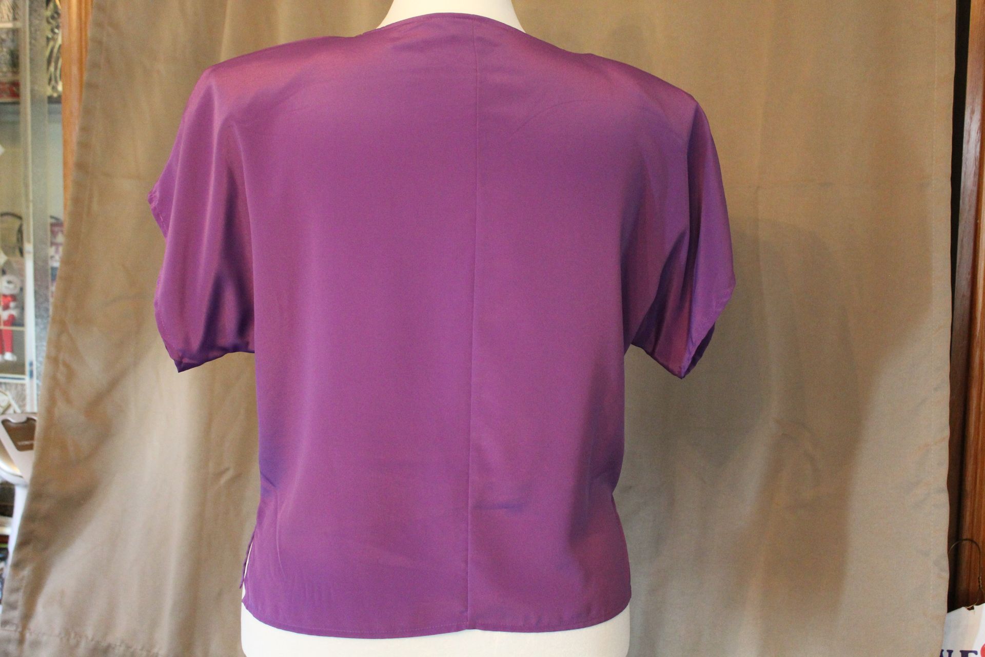 Purple short-sleeve T-shirt hanging against a beige backdrop with a white heart tag at the collar