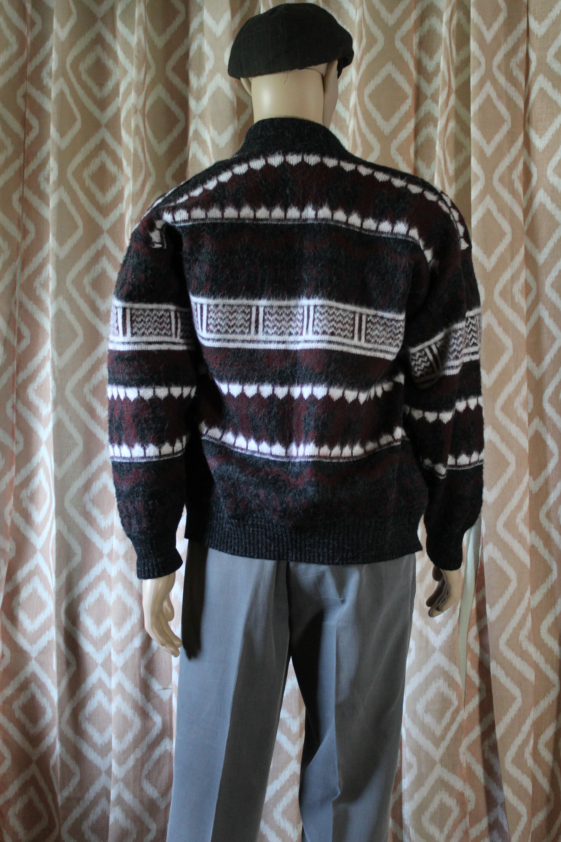 Person seen from behind wearing a black patterned sweater, gray pants, and a black cap, standing indoors.